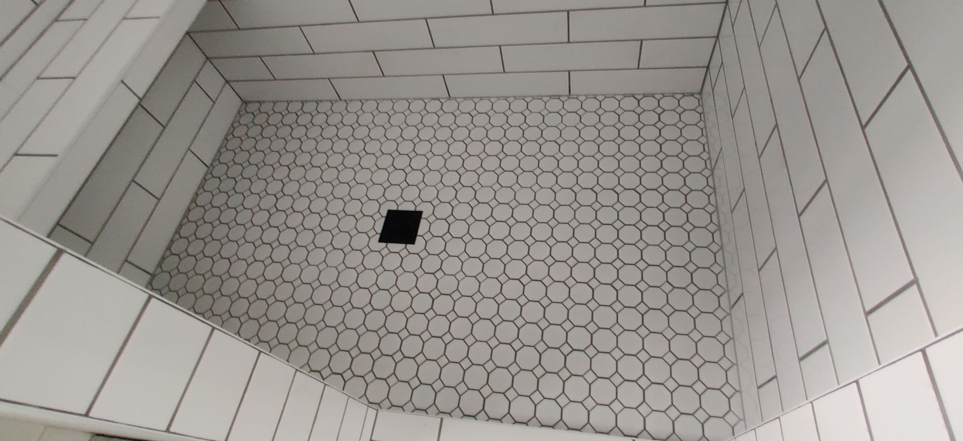 Tiled shower floor with small hexagonal tiles and a square drain in the center.