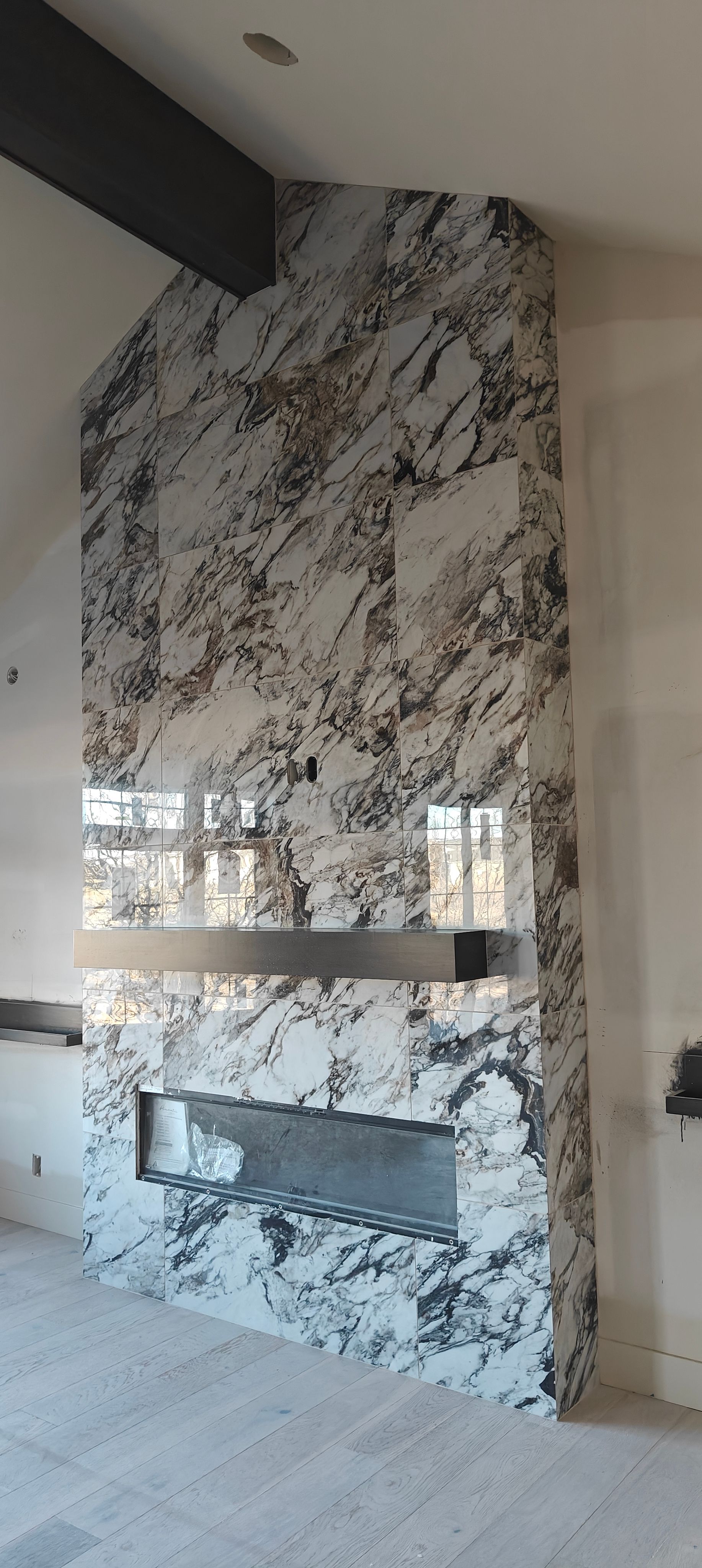Marble-tiled fireplace wall with a built-in rectangular opening and black beam above.