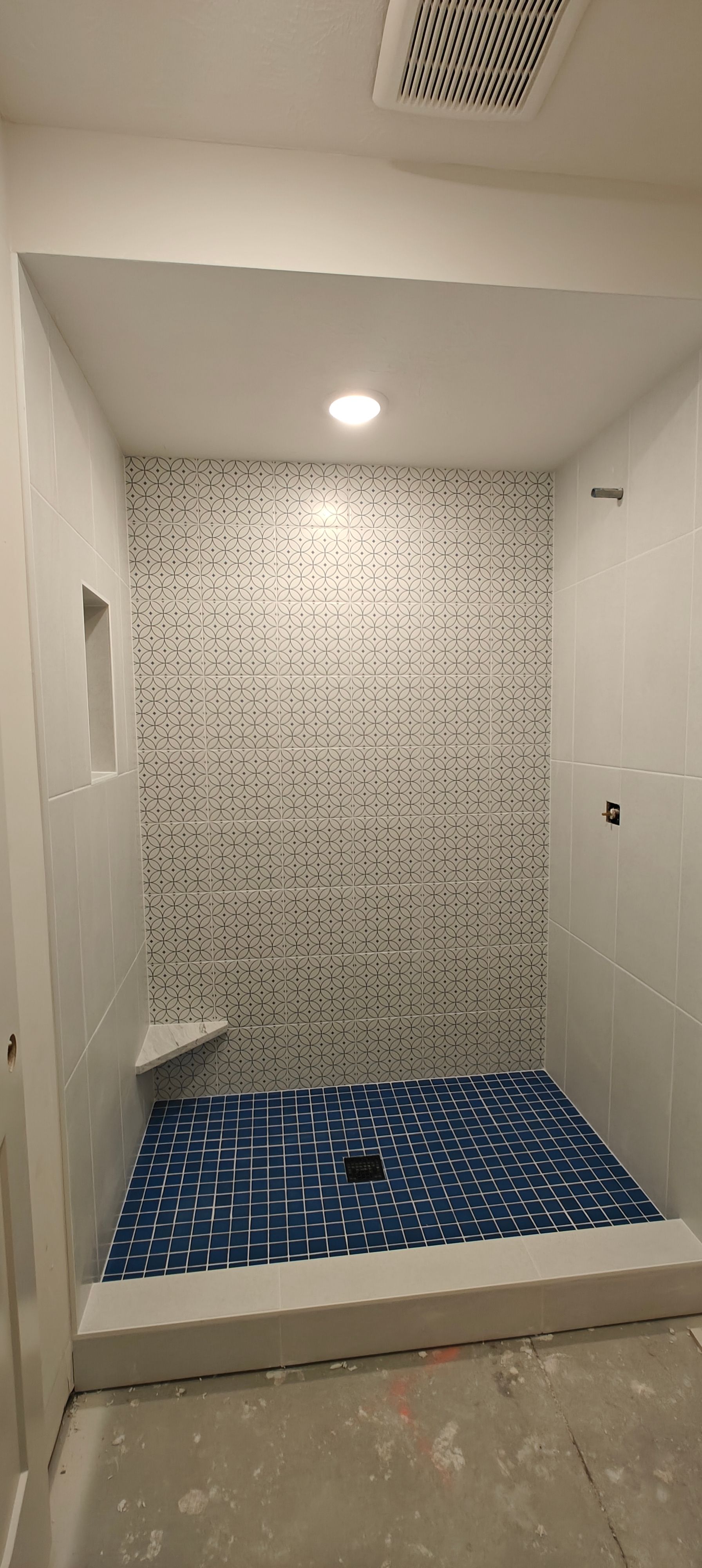Empty tiled shower stall with blue mosaic floor, white walls, and a recessed light.