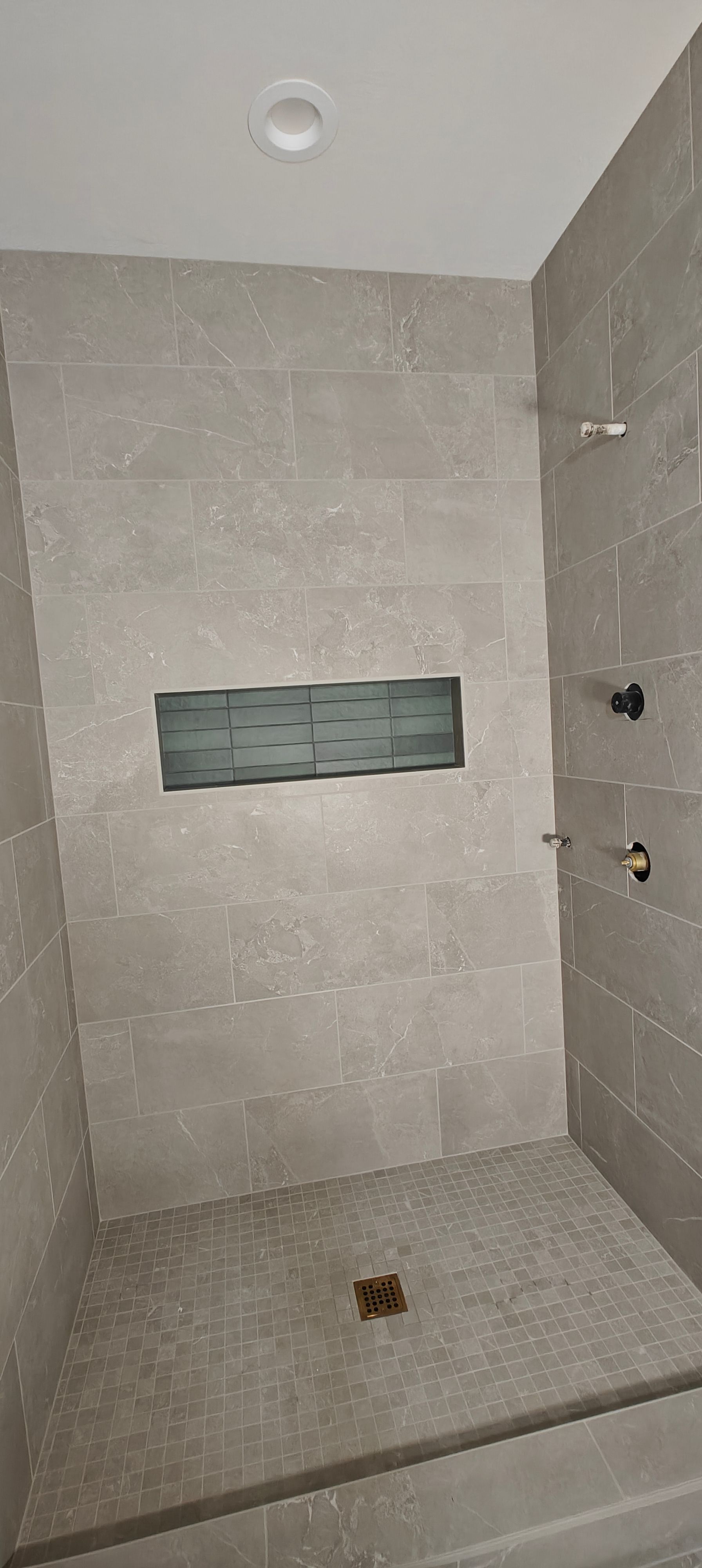 Empty tiled shower with built-in niche and floor drain, viewed from the doorway.