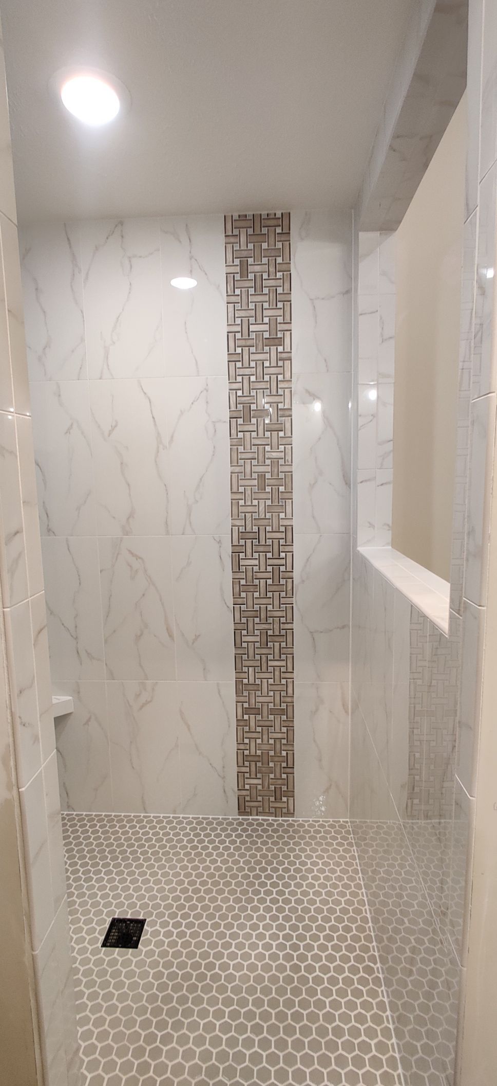 Modern tiled shower with white walls, marble-look panels, and a narrow mosaic accent strip.