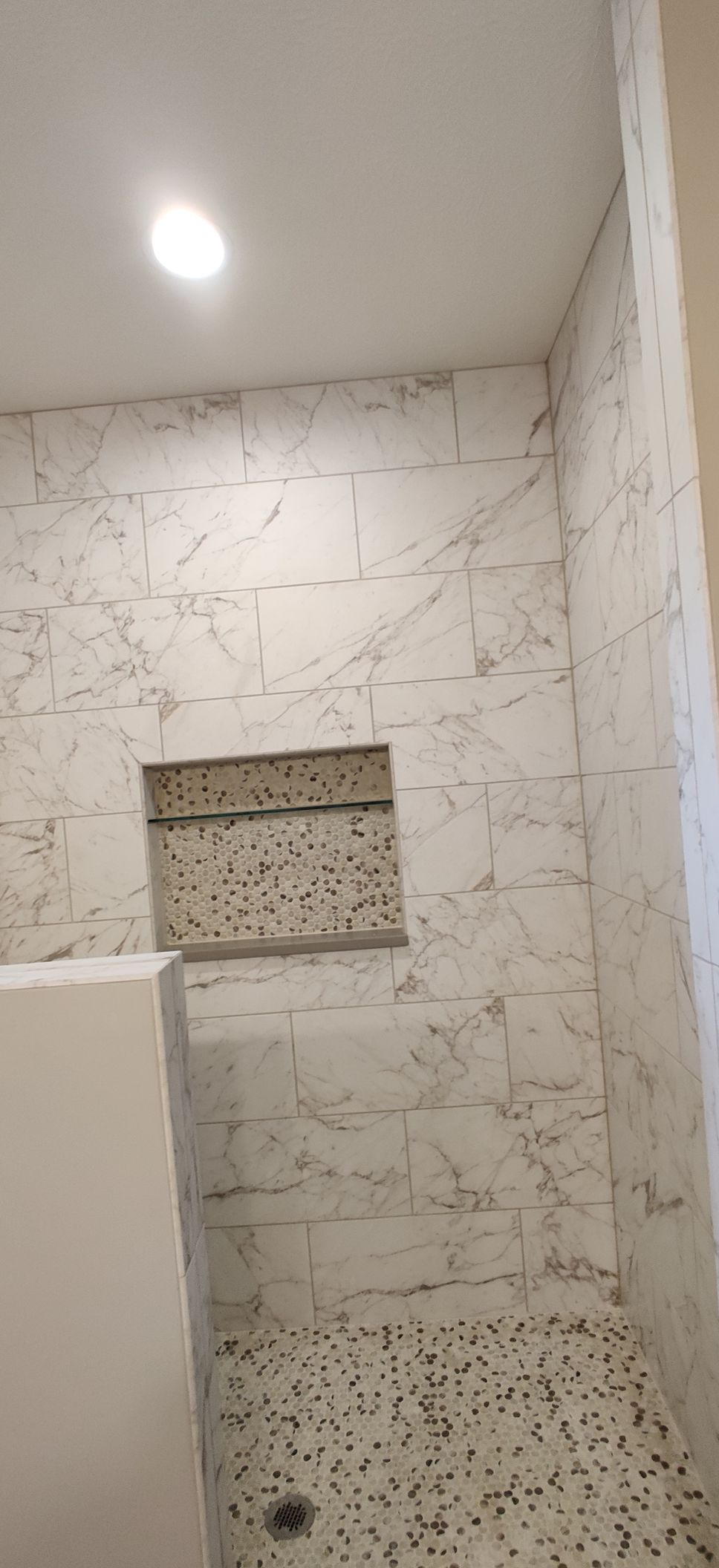 Small tiled bathroom with a wall niche, light ceiling, and pebble-style shower floor.