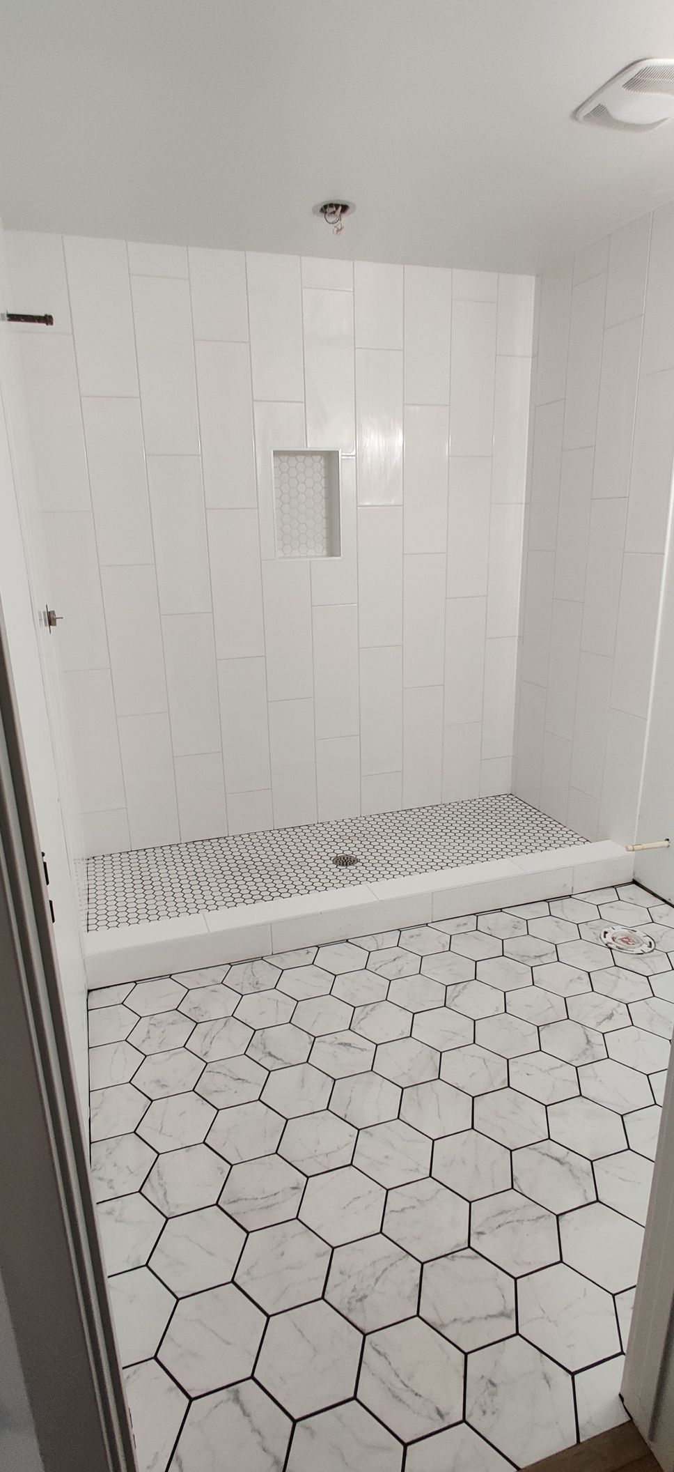 White tiled shower and bathroom floor with black hexagon pattern and a wall niche.