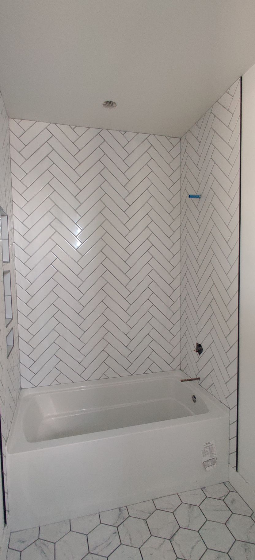 Small white tiled bathroom with a bathtub and hexagon-tile floor, under construction or newly renovated.