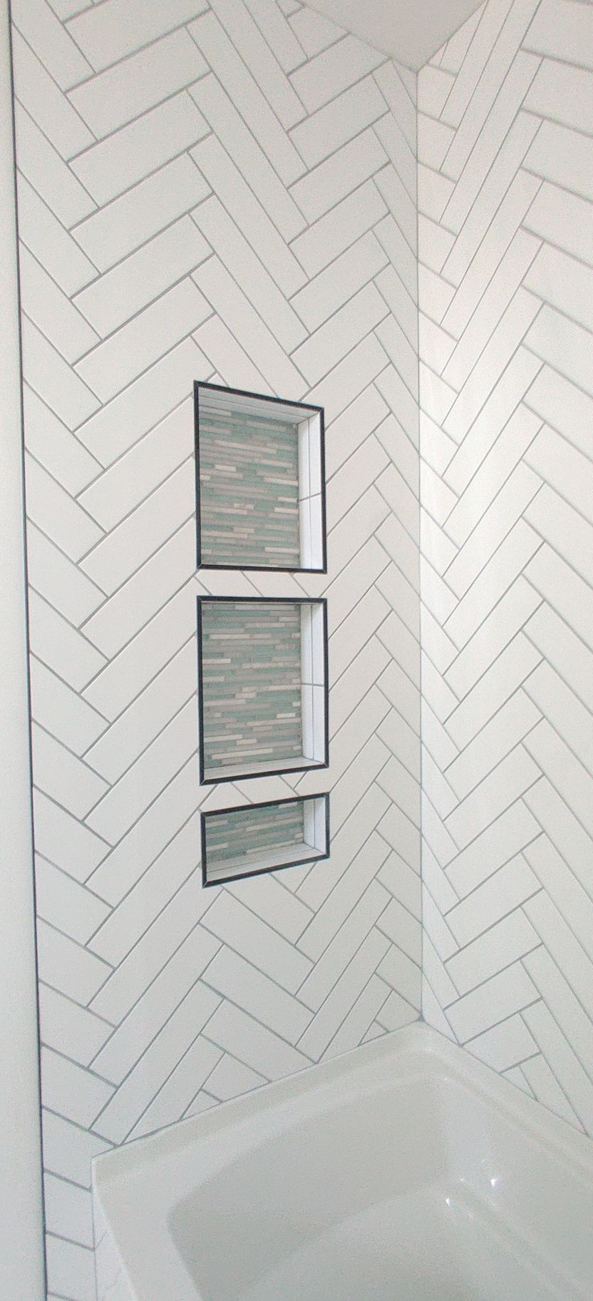 White chevron-tile shower wall with three narrow windows above a bathtub.