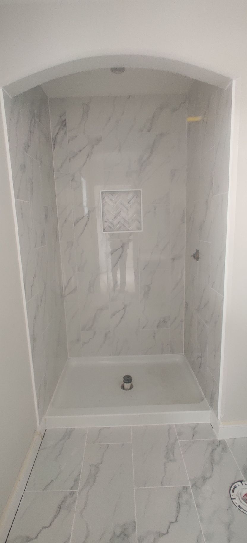 Empty tiled shower alcove with marble-look walls, built-in niche, and faucet fixture.