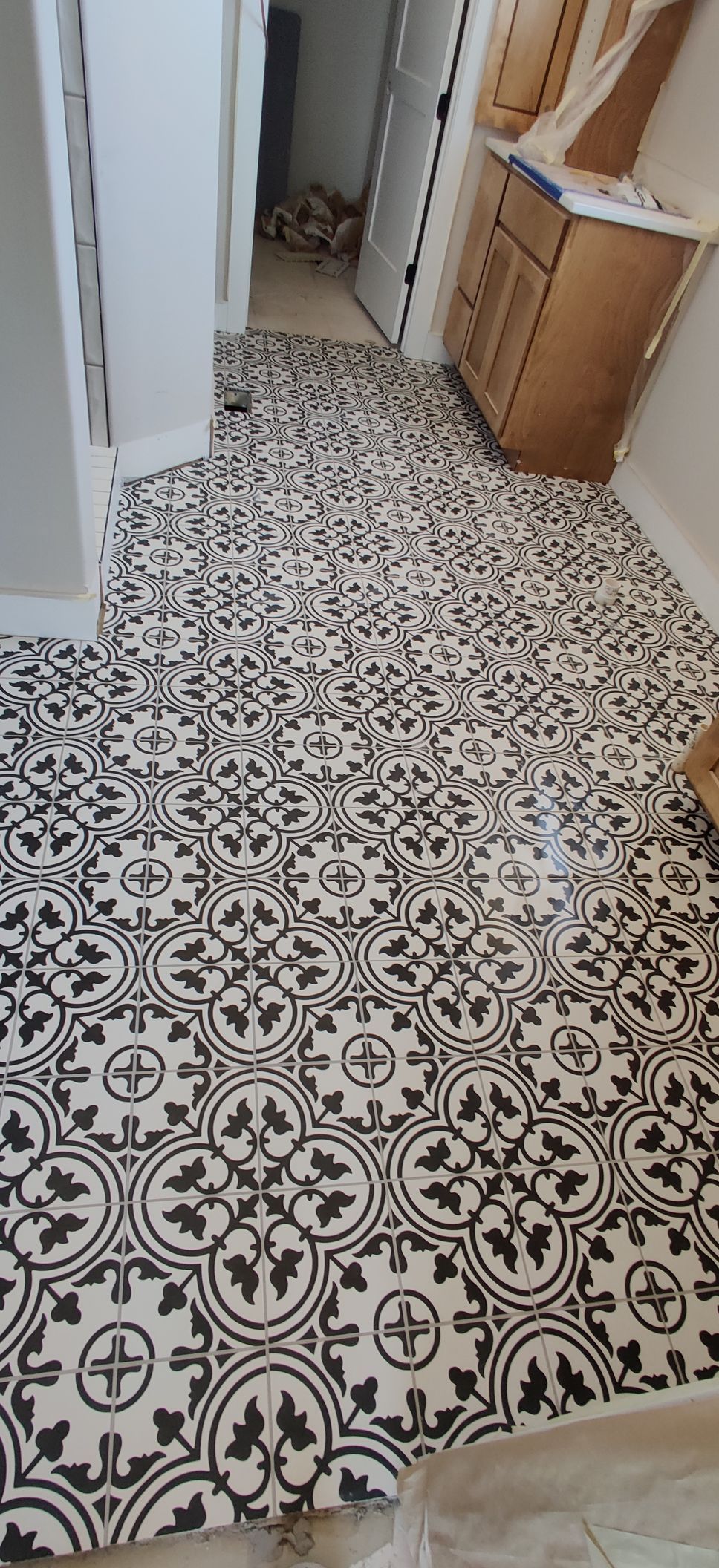 Narrow hallway with black-and-white patterned tile floor and light-colored walls and cabinets.