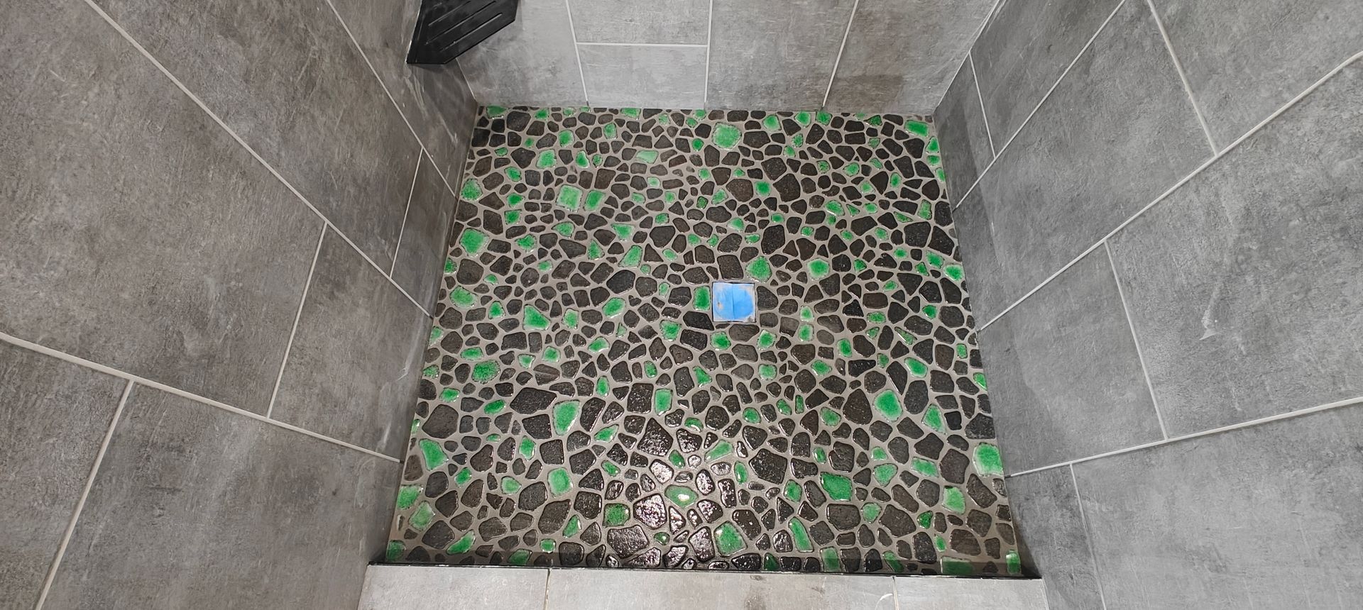 Tile-lined shower floor with a patterned brown-and-green center and a blue drain cover.
