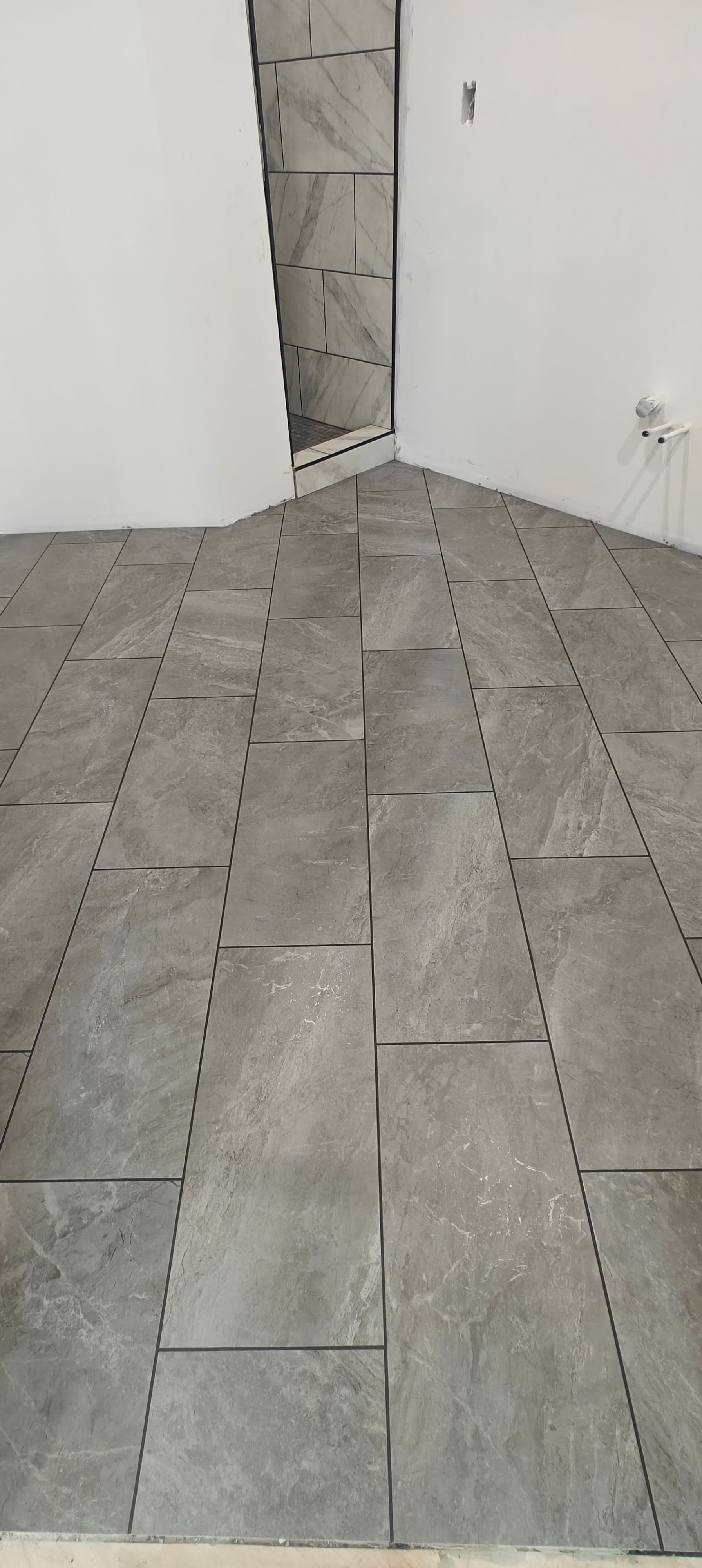 Empty room with gray tile floor, white walls, and a narrow doorway in the back corner.