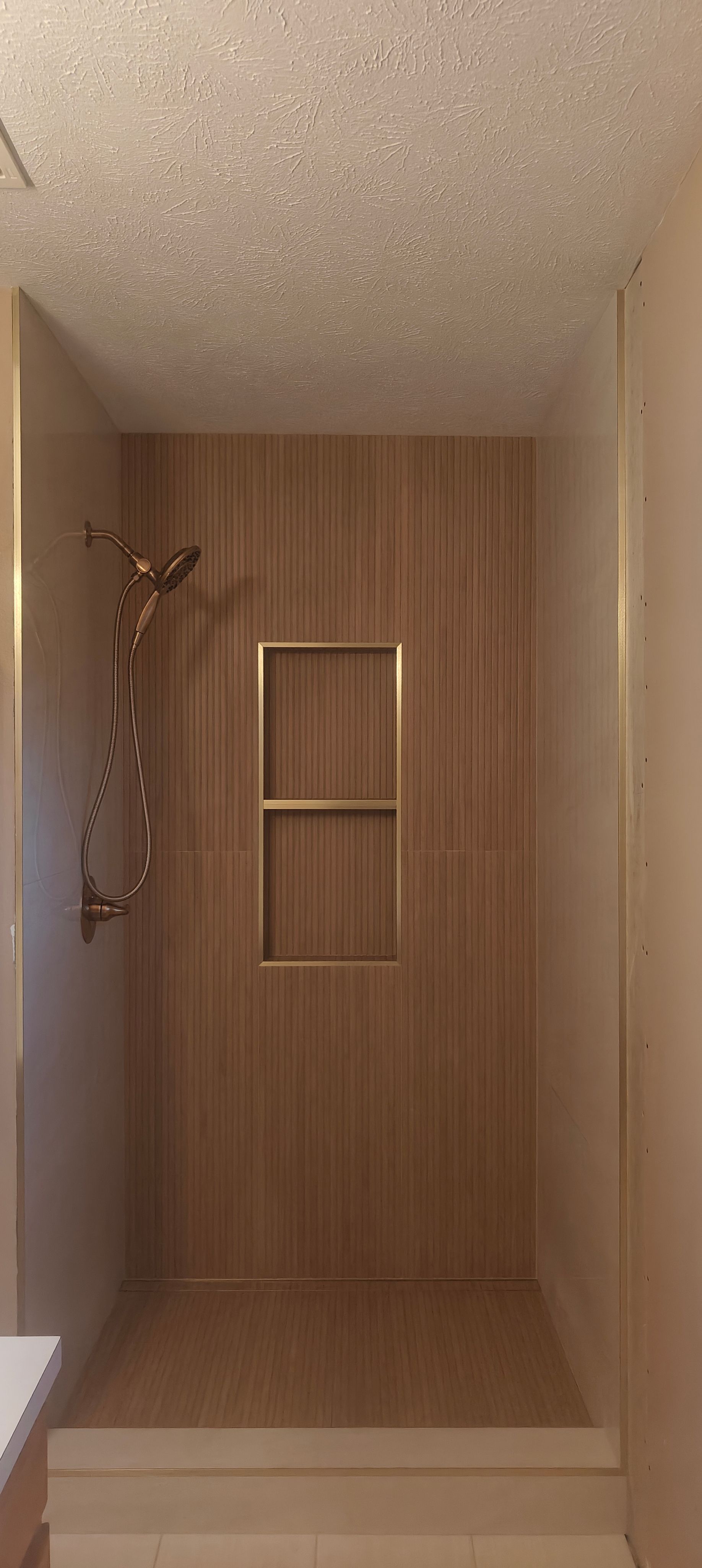 Wood-paneled walk-in shower with a small wall shelf and brass shower fixture on the left.