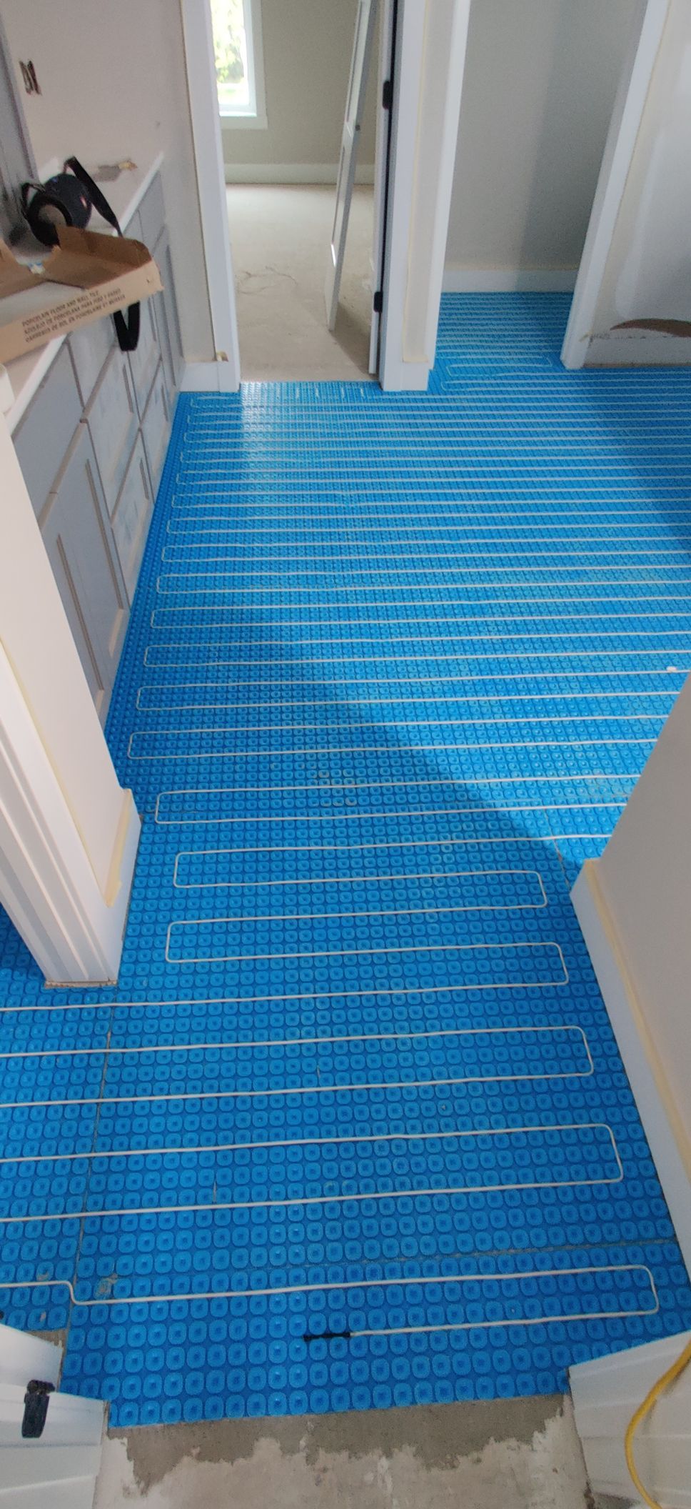 Blue protective floor covering in a hallway with white doors and cabinets nearby.
