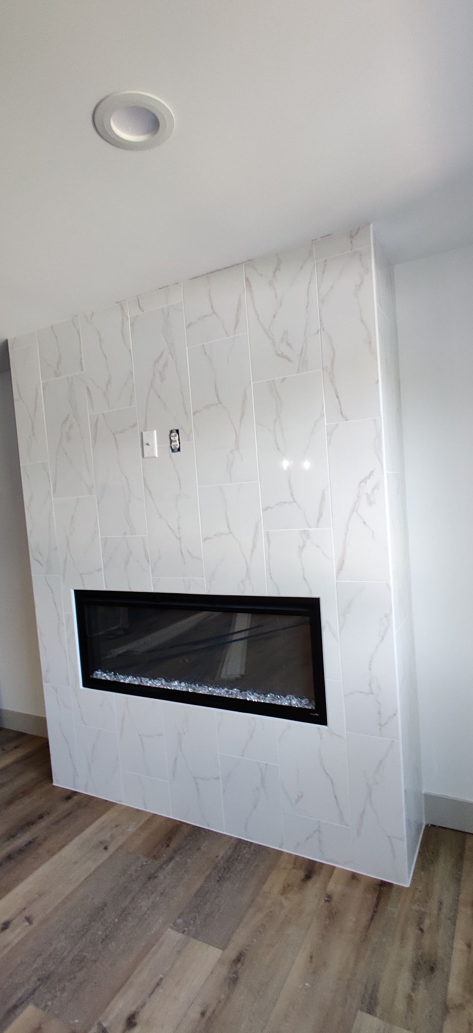 Modern white marble fireplace wall in a room with wood flooring and a recessed black firebox.