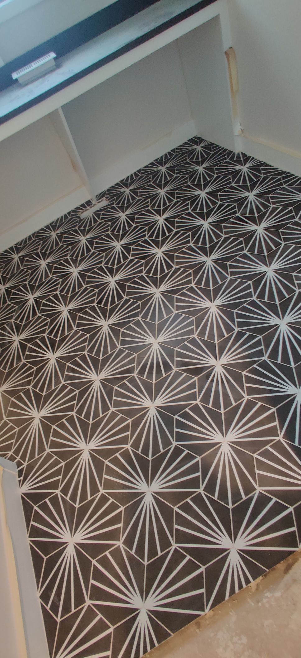 Small room with black-and-white geometric patterned flooring under white cabinets and a wall shelf.