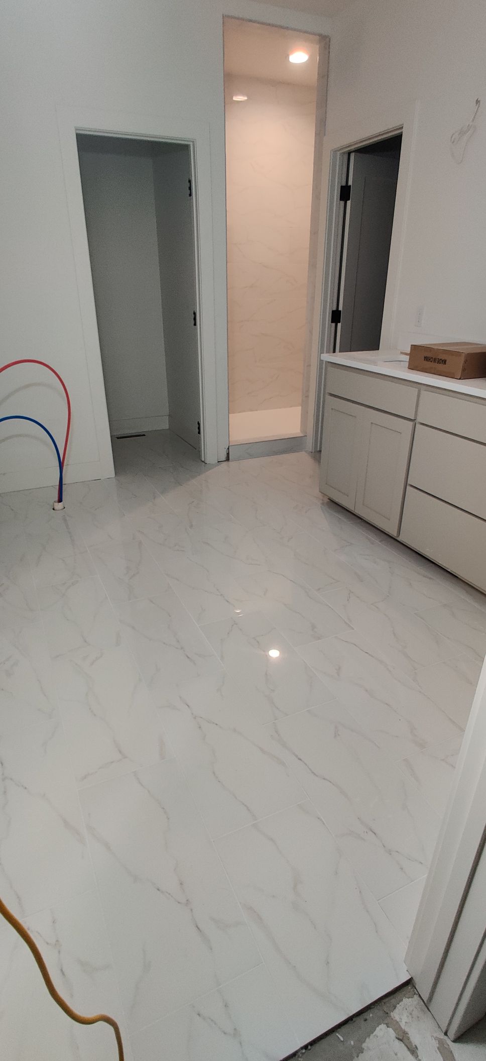 Empty white-tiled room with open doorways, recessed lights, and a white cabinet along the wall.