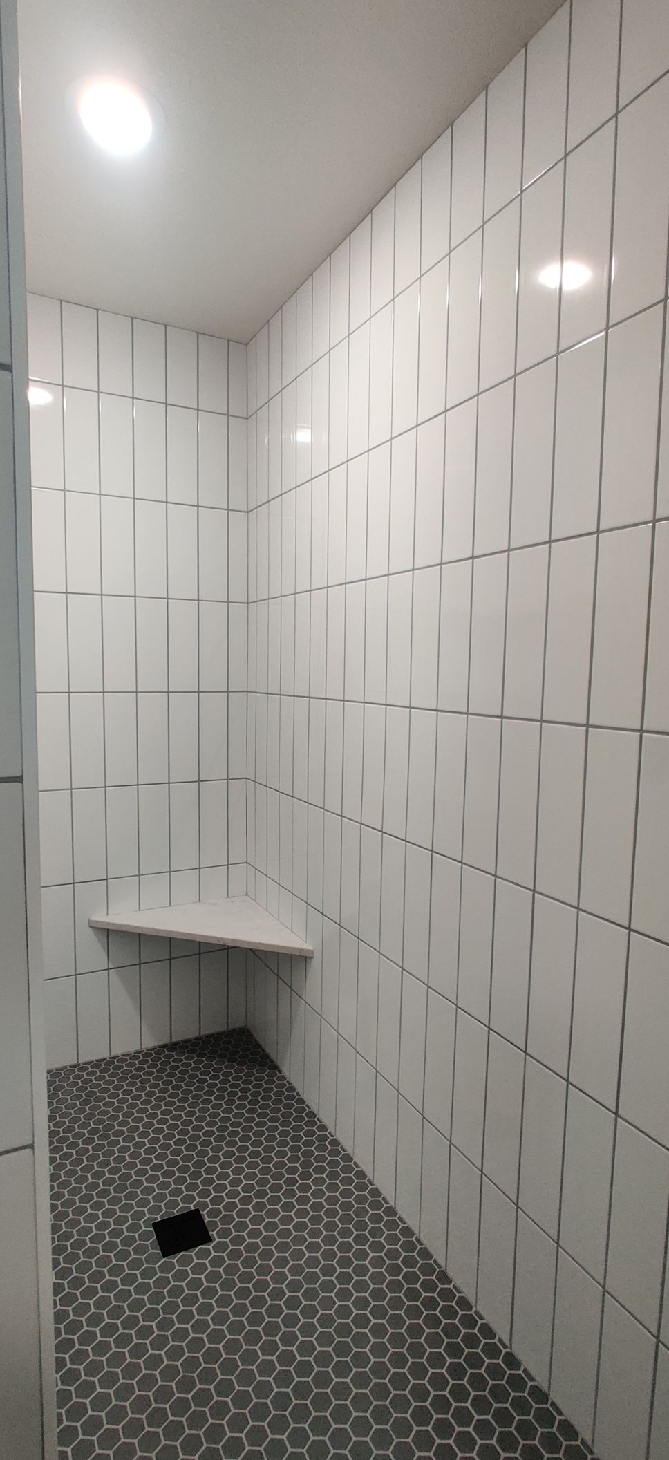 Narrow tiled restroom stall with a small corner sink and dark patterned floor.