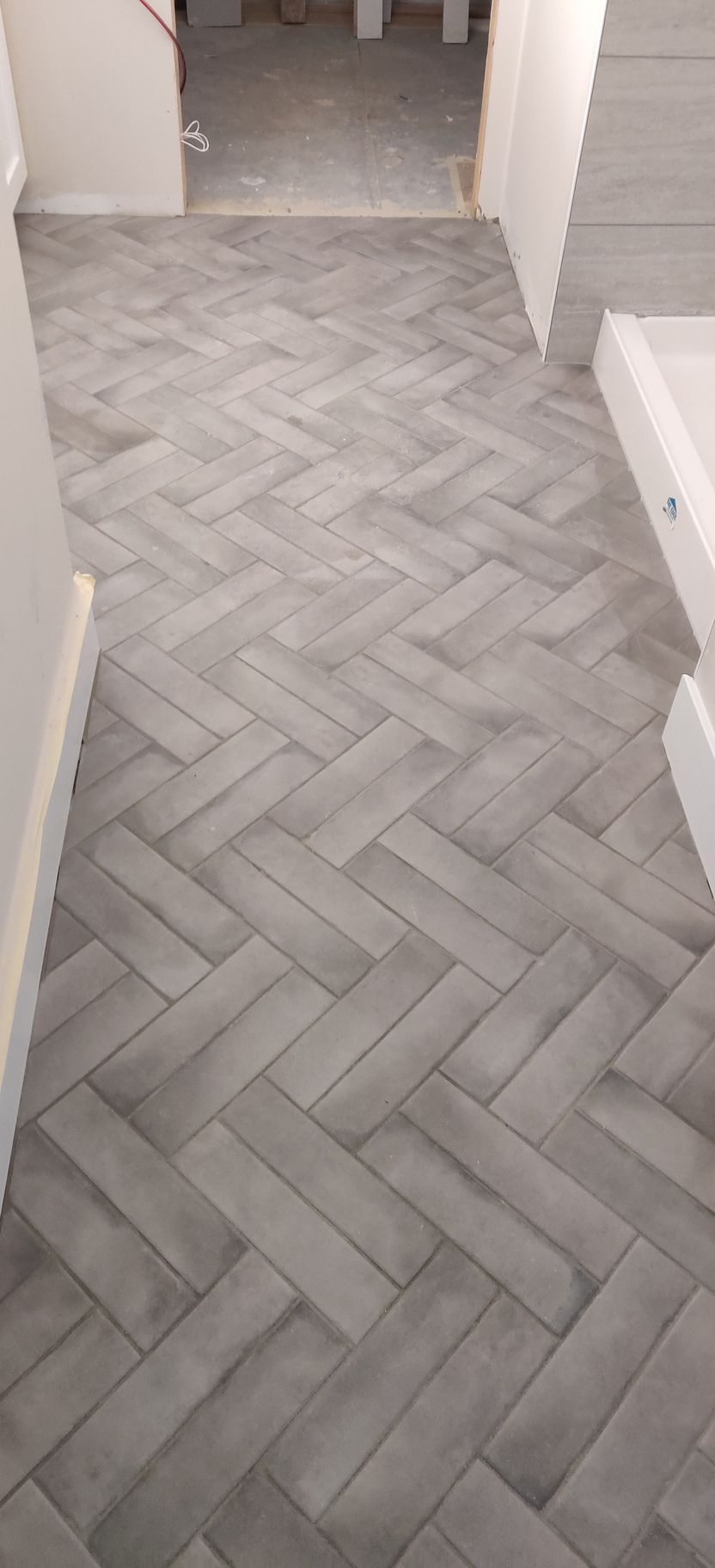 Gray herringbone tile floor in a hallway leading to a doorway.