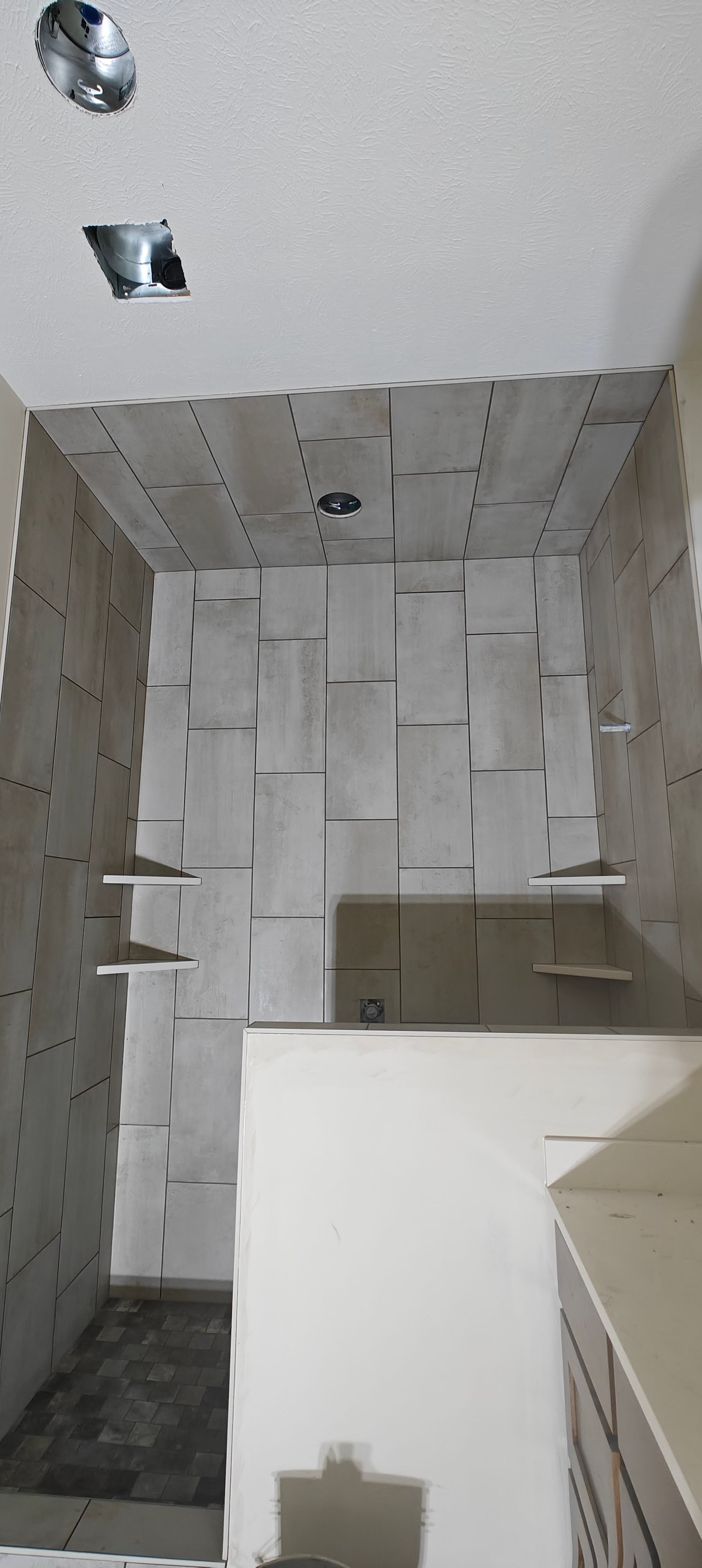 Tiled bathroom shower wall with a small ledge and white ceiling, viewed from below.