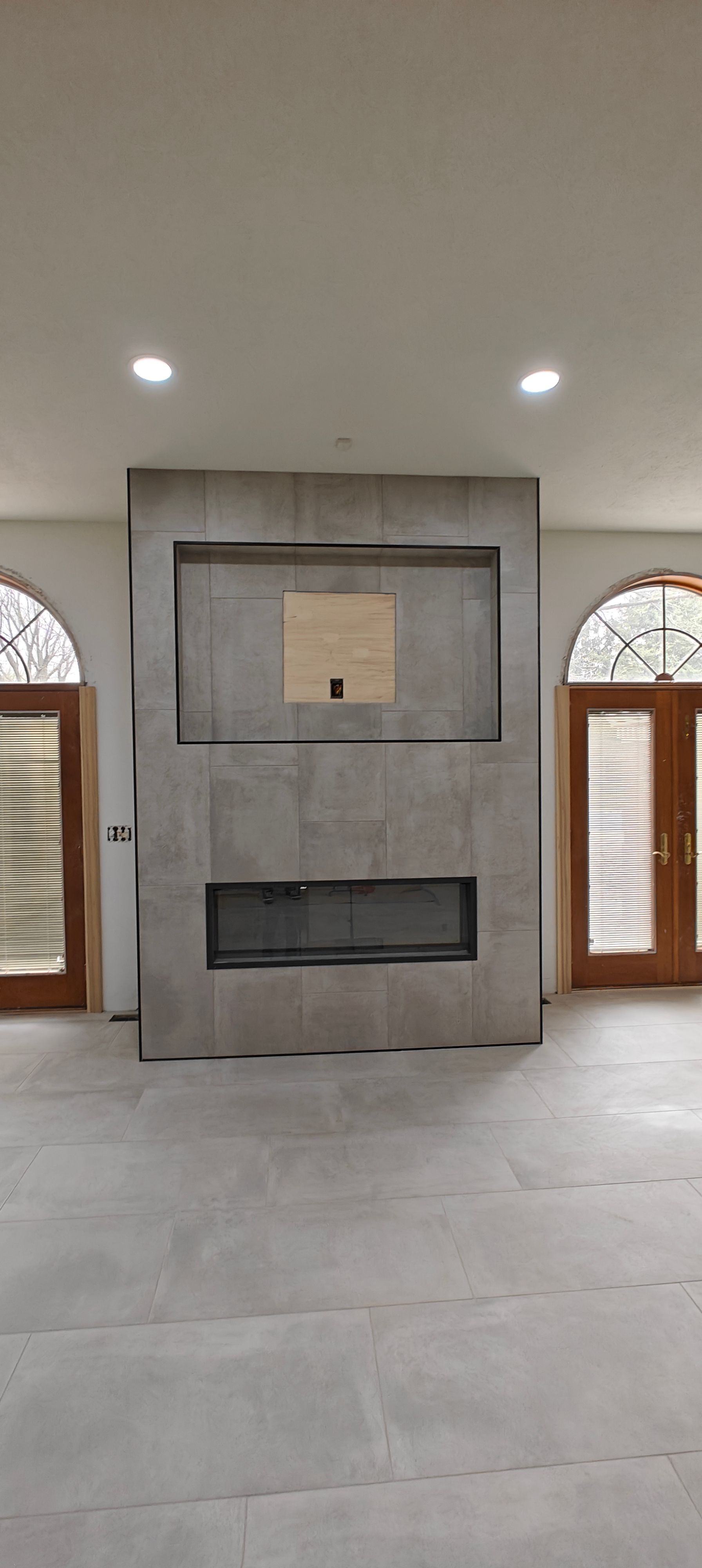 Modern living room with a gray fireplace wall and wood-trimmed windows on both sides.