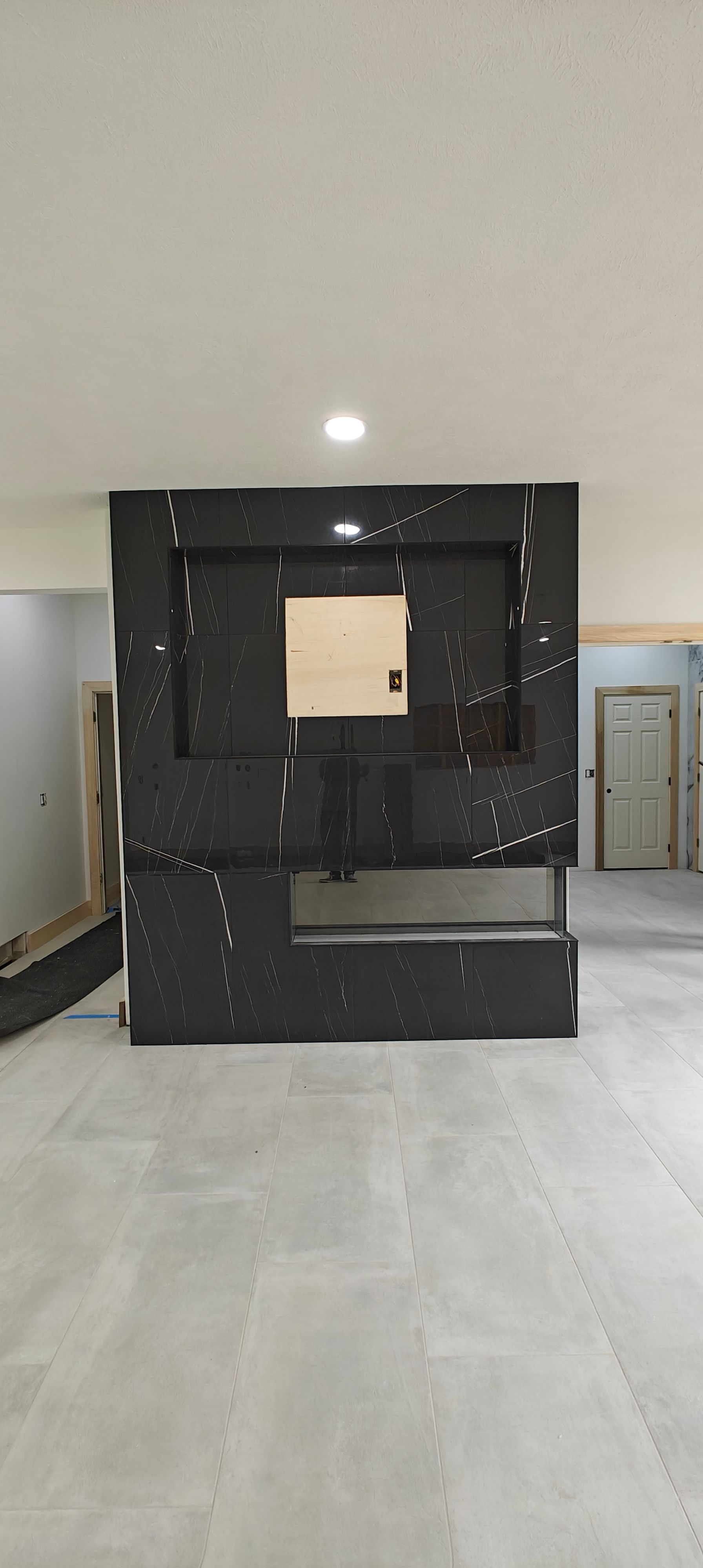 Black modular wall display in a gray room with a small square opening and overhead light.