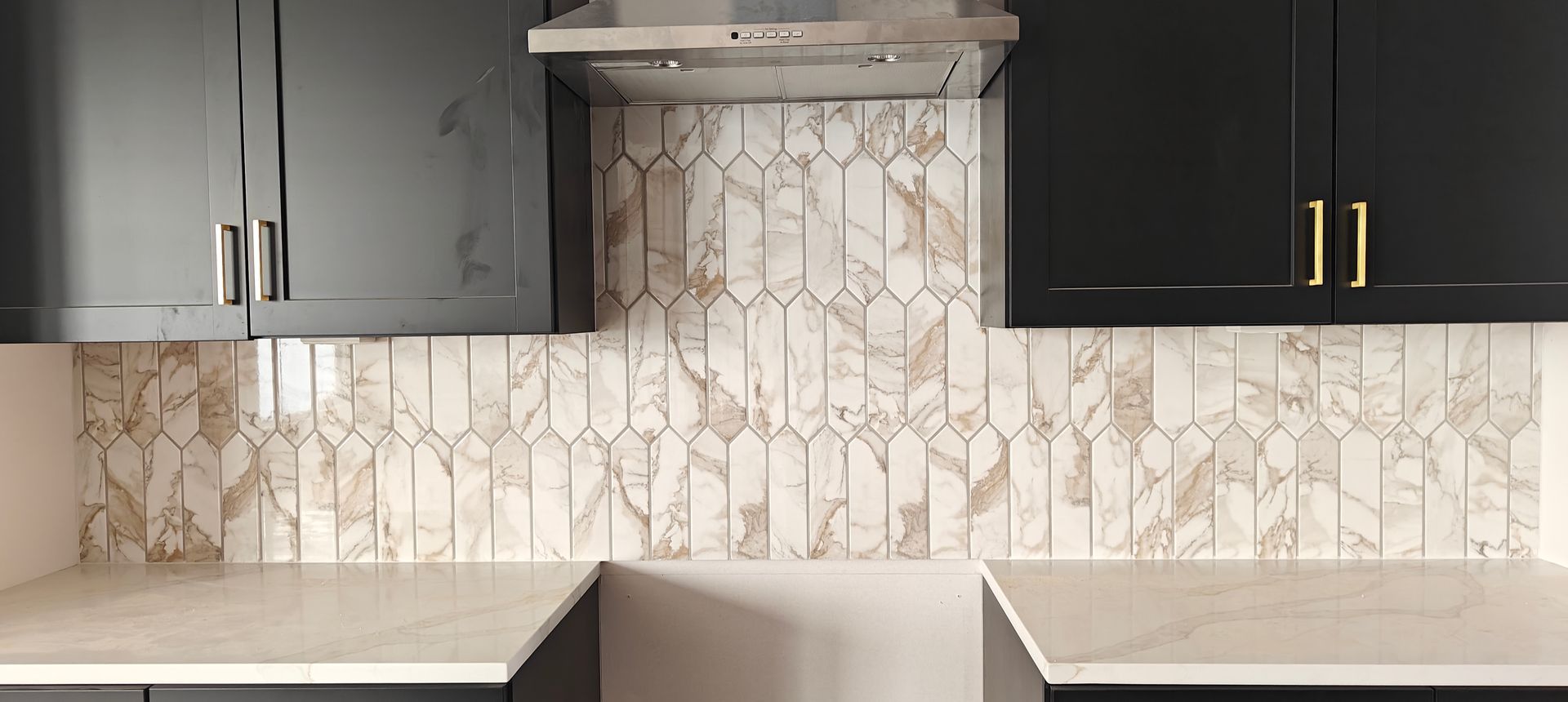 Modern kitchen with dark cabinets, marble backsplash, range hood, and light countertops.