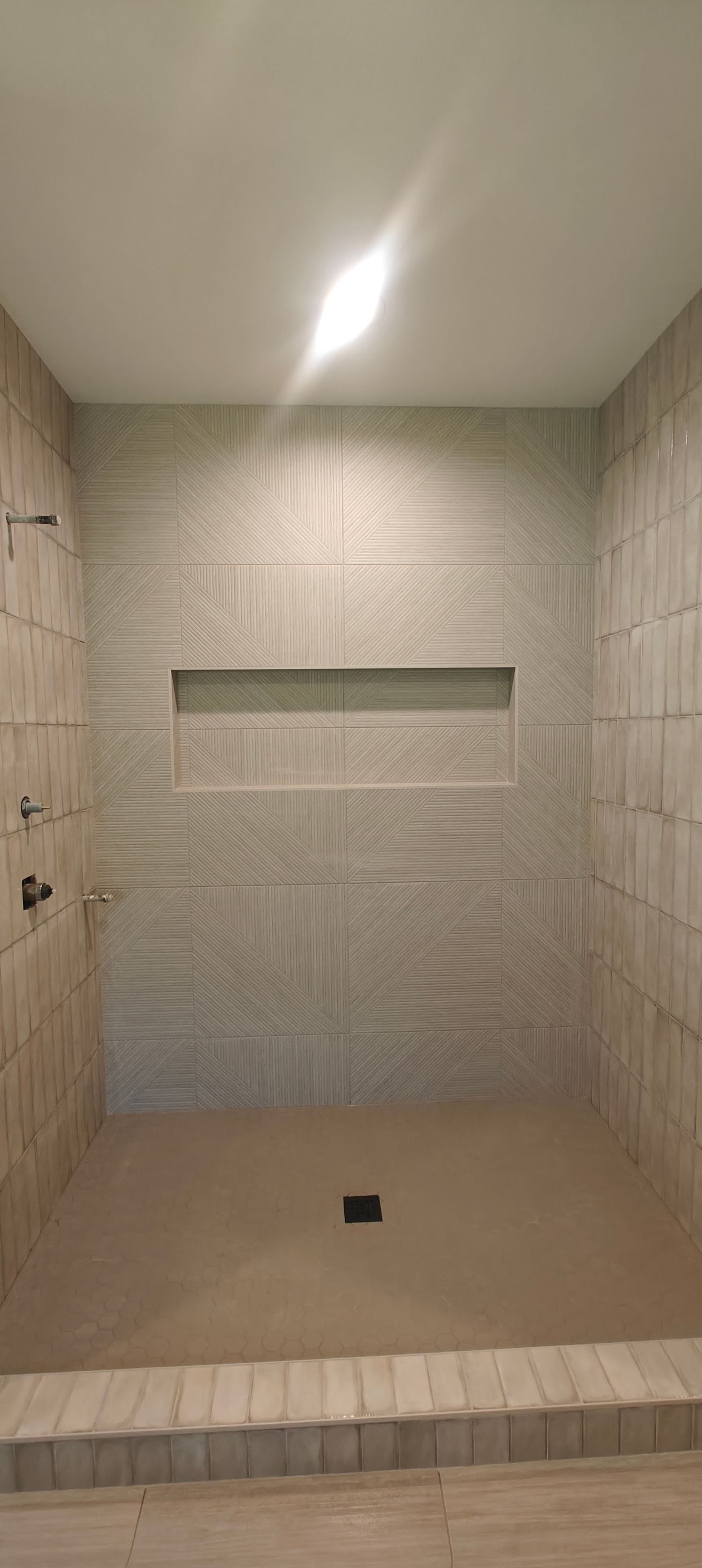 Empty tiled shower stall with a bench, beige walls, and built-in niche.