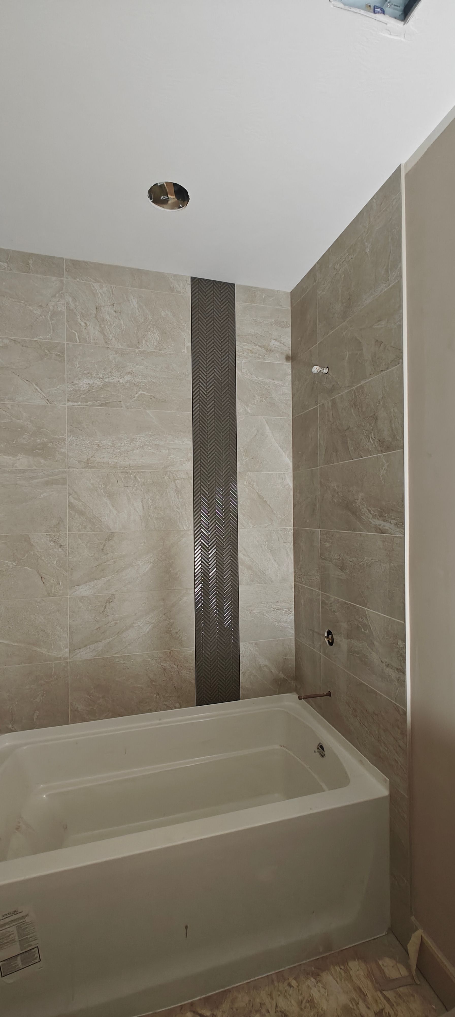 Empty tiled bathtub in a small bathroom with beige and white walls and a ceiling light opening.