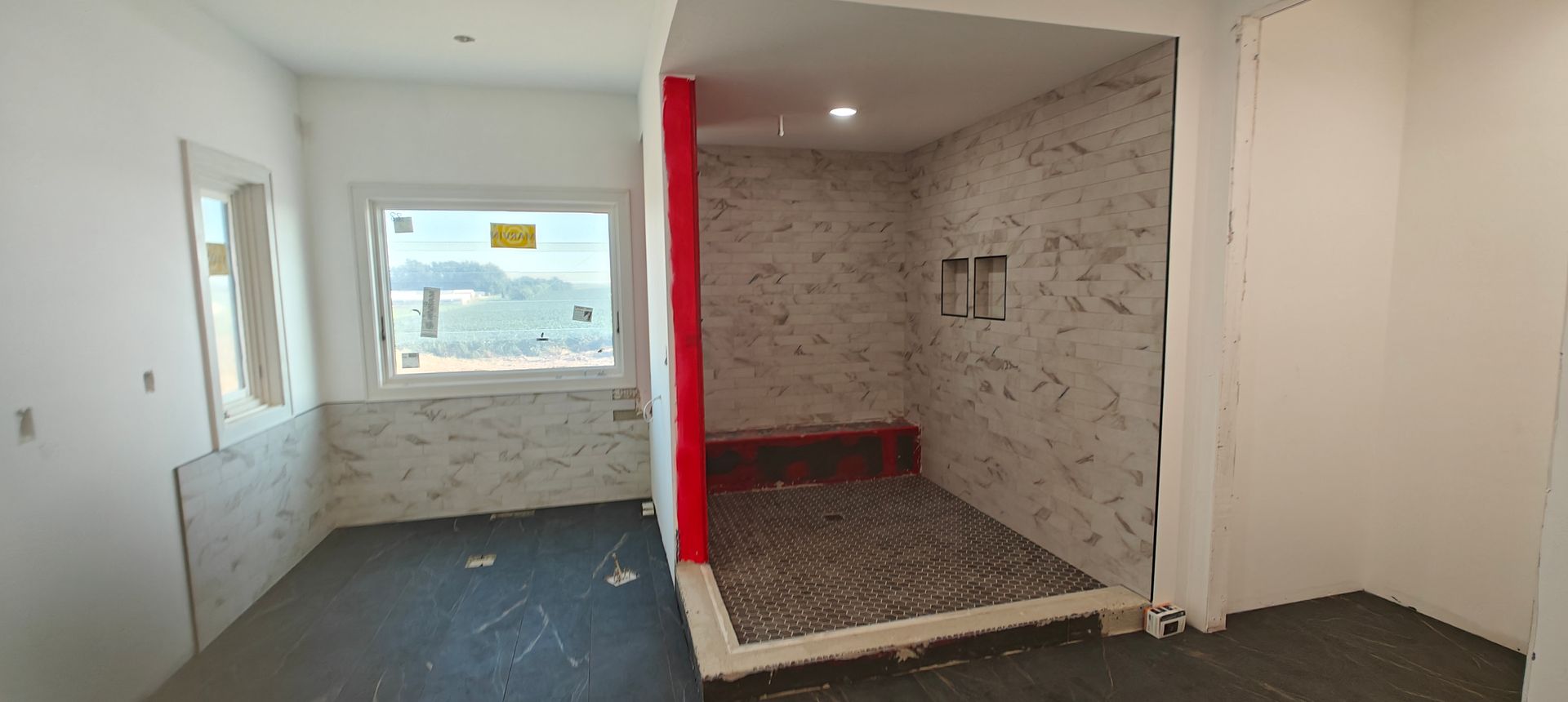 Empty white room with a built-in tiled shower nook and a window overlooking the street.