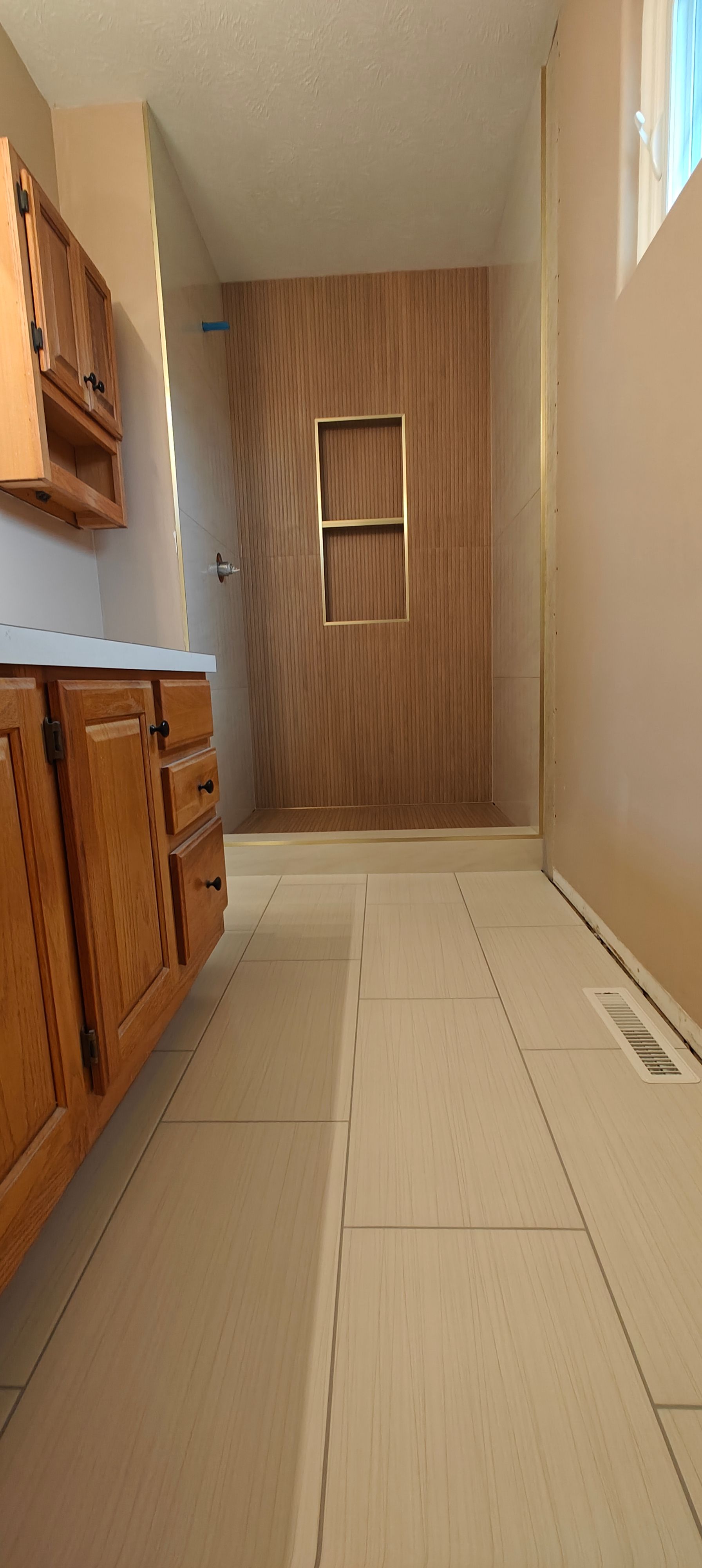 Narrow bathroom with beige tile floor, wooden cabinets, and a wood-paneled wall with two small windows.