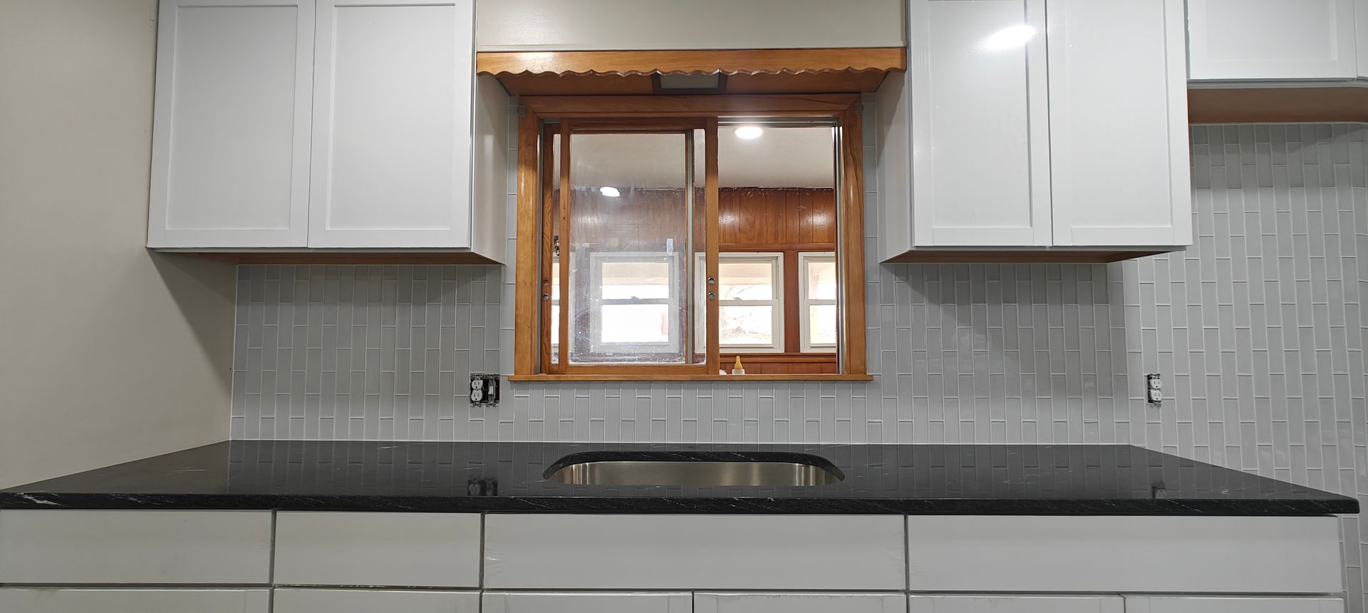 Modern kitchen with white cabinets, black countertops, and a window over the sink.
