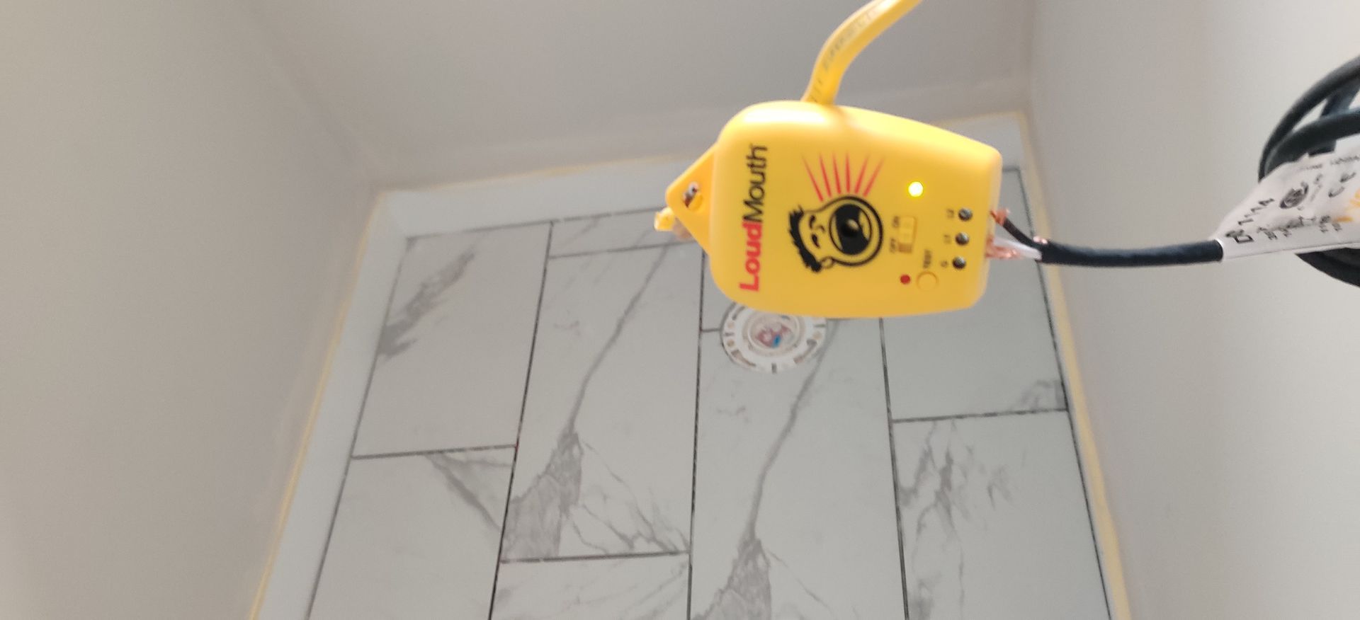 Yellow bottle attached to a rod, held over a tiled surface with a circular drain opening.