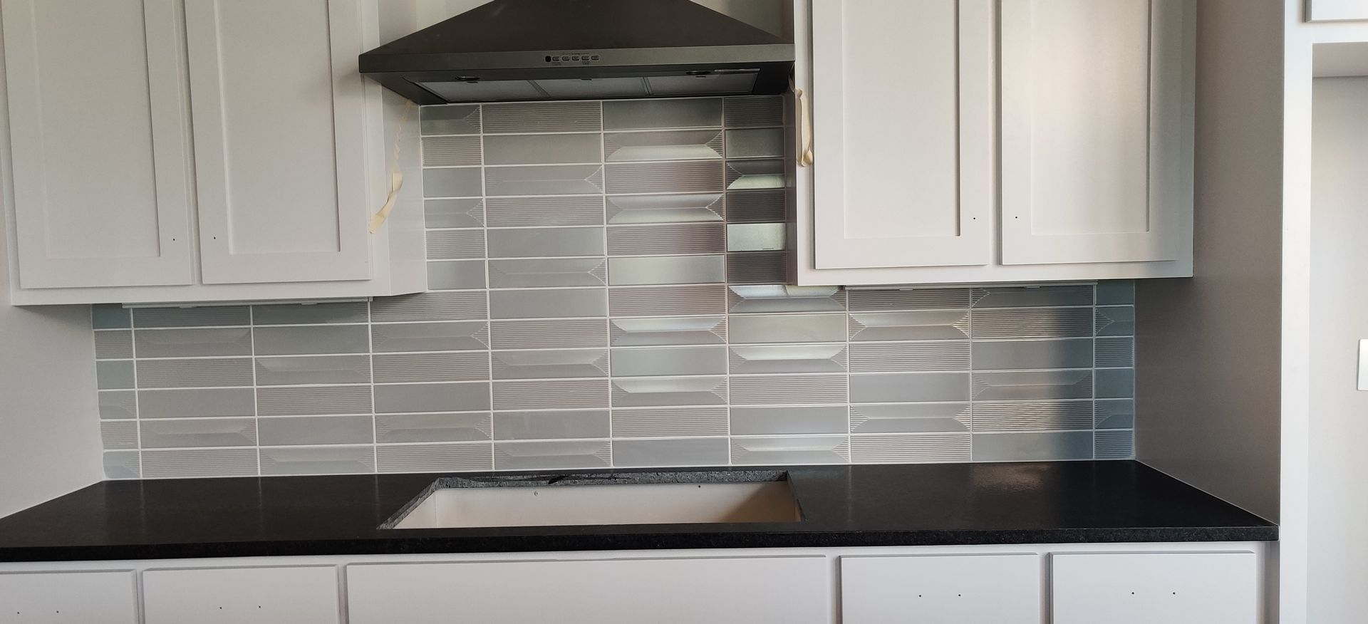 Modern kitchen with white cabinets, gray tile backsplash, black countertops, and a central stovetop range.