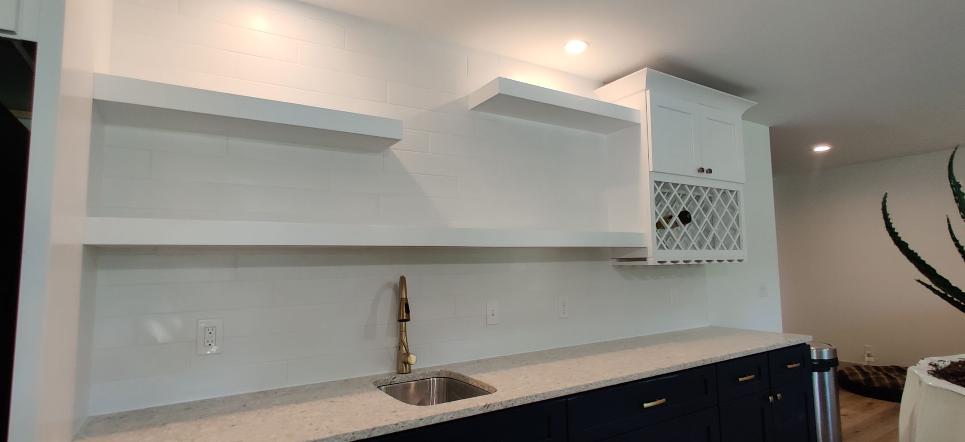 Modern kitchen with white shelves, sink, and dark blue cabinets under bright lighting.