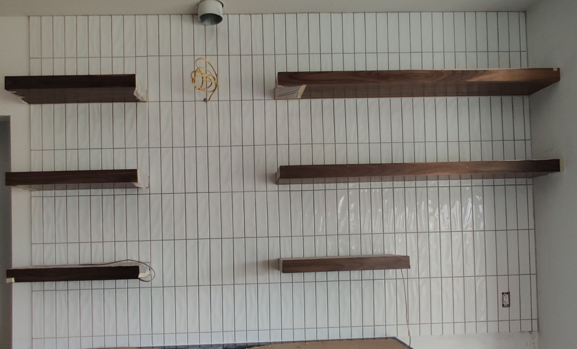 Wall-mounted wooden shelves on a white slatted wall with a small hanging ornament at the center.