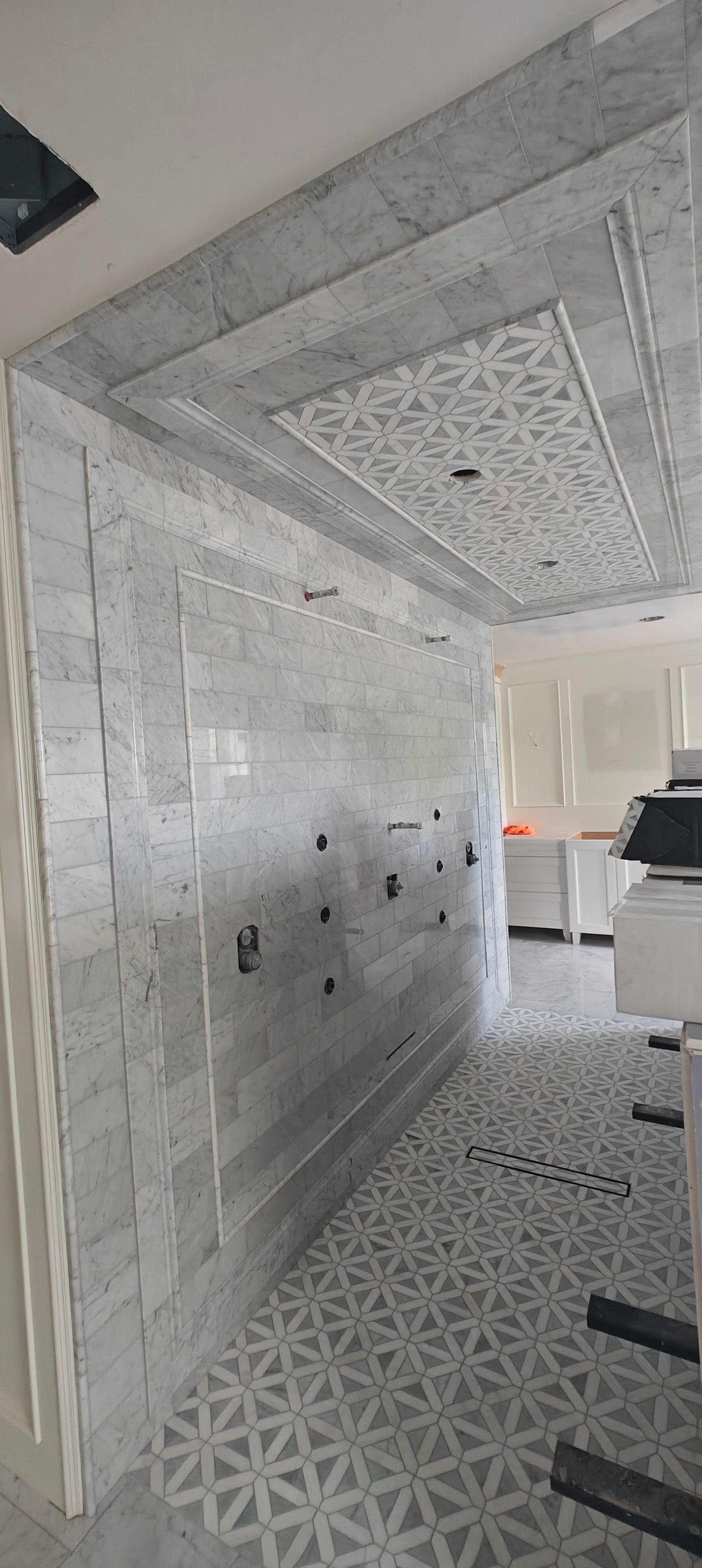 Narrow tiled hallway under construction with gray patterned walls, ceiling, and floor, leading to a bright opening.