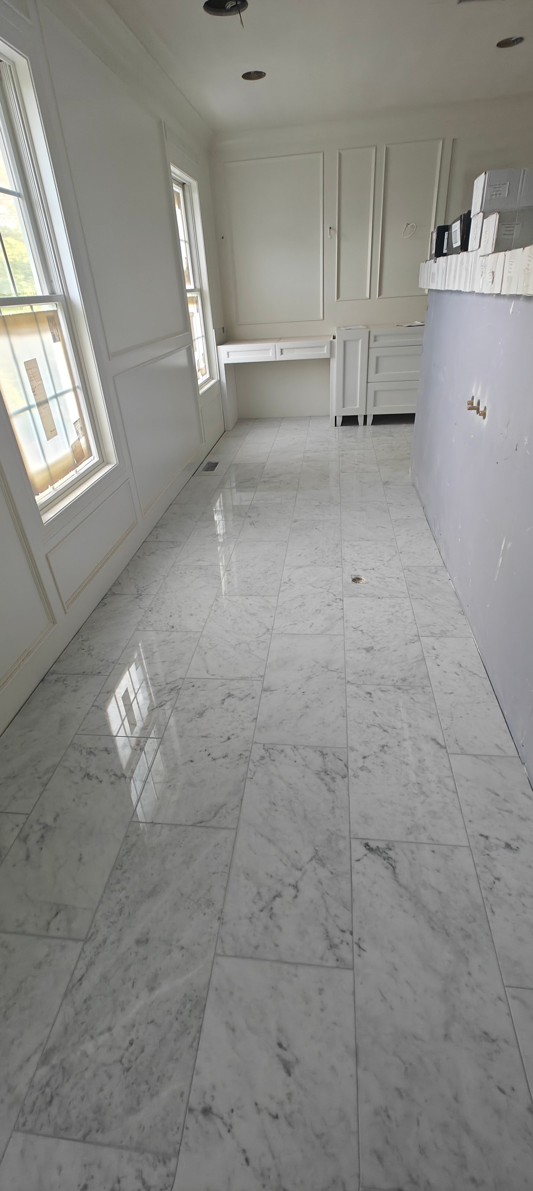 Bright white modern kitchen with marble floor, tall cabinets, and large windows letting in natural light.