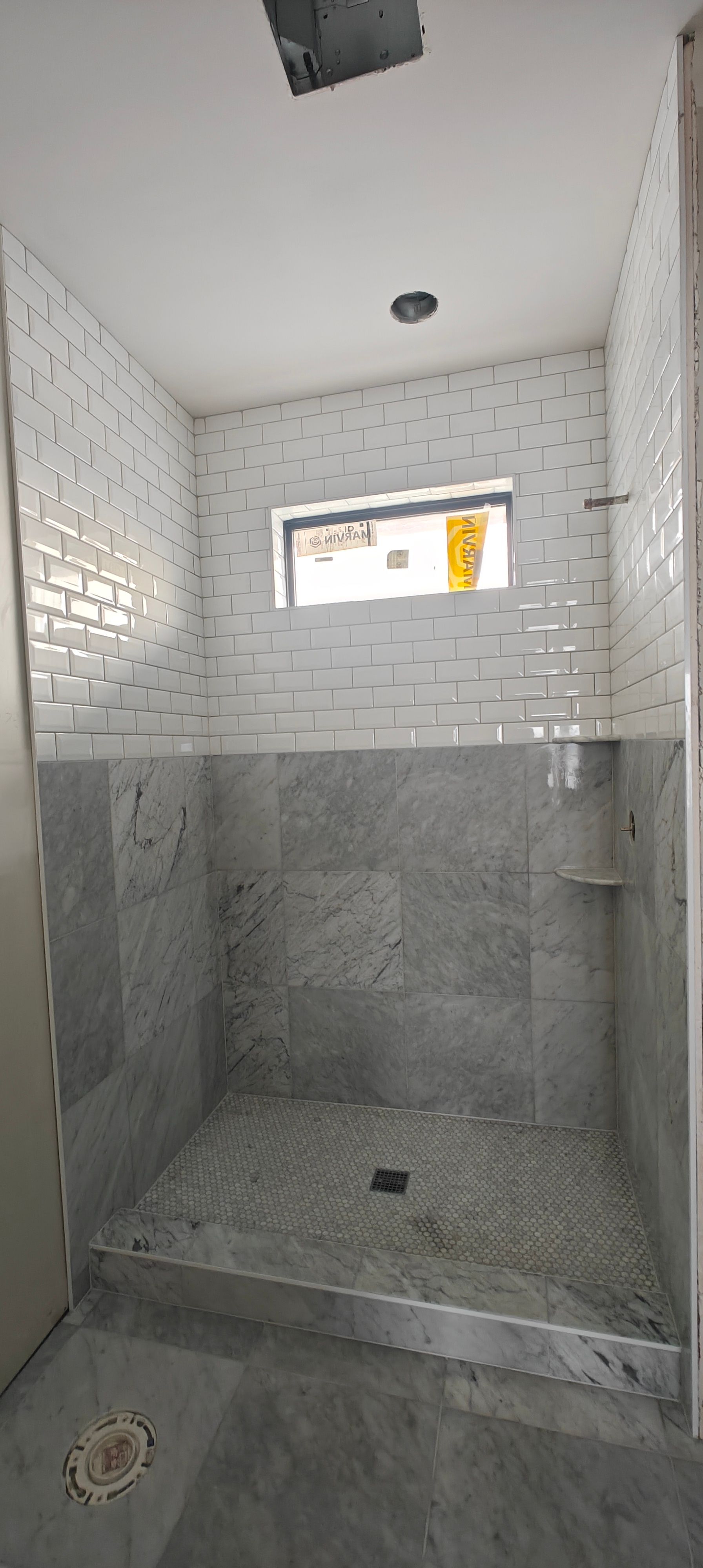 Small tiled bathroom shower with gray stone walls, white subway tile, and a small window.