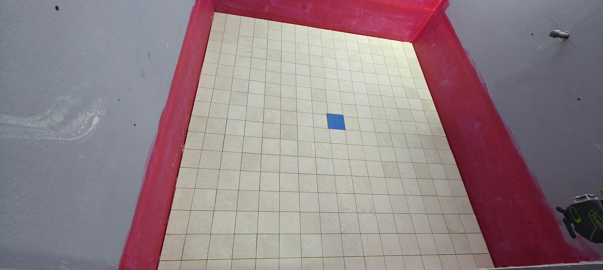 Red-bordered tray with a beige tiled floor and a small blue square tile near the center.