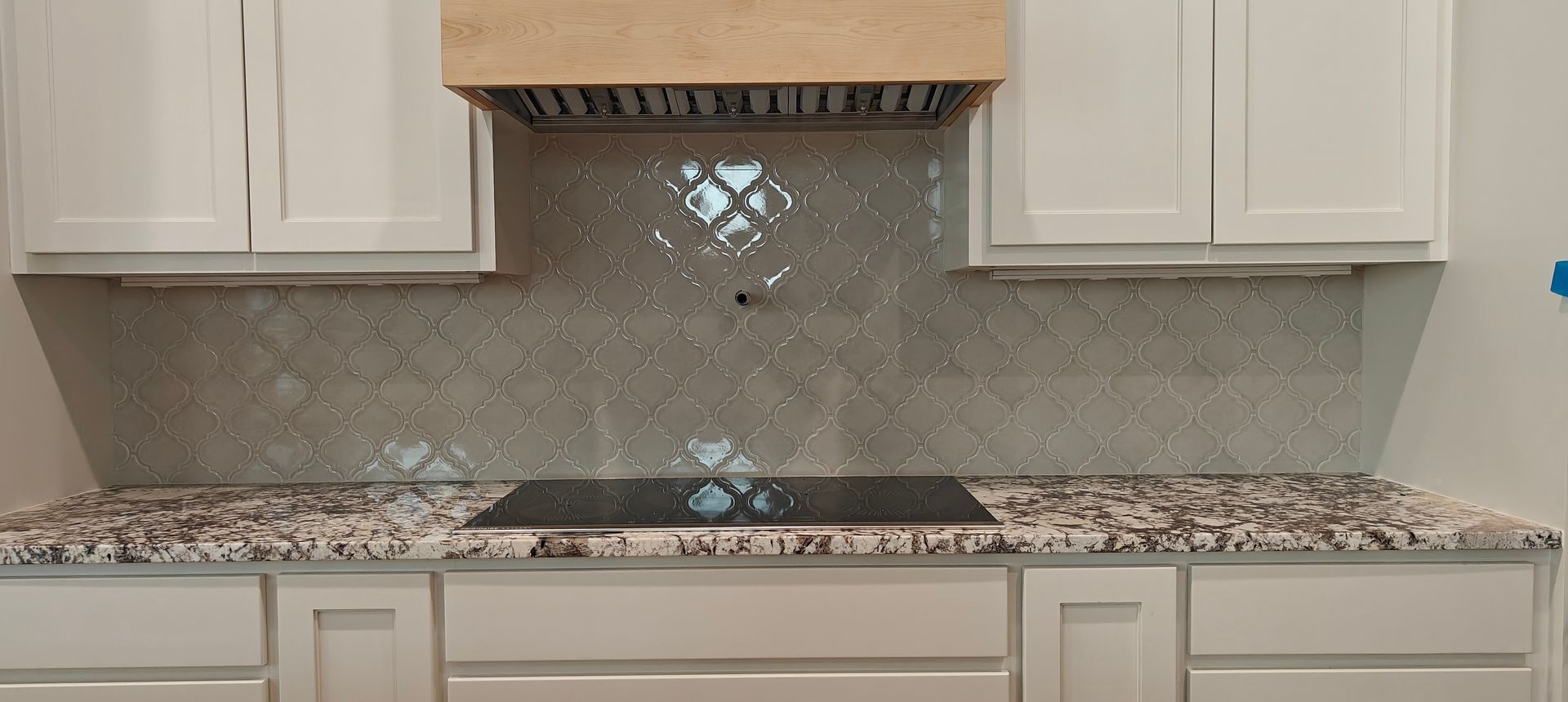 Kitchen backsplash with white cabinets, speckled granite countertop, and mosaic tile accent behind a range hood.