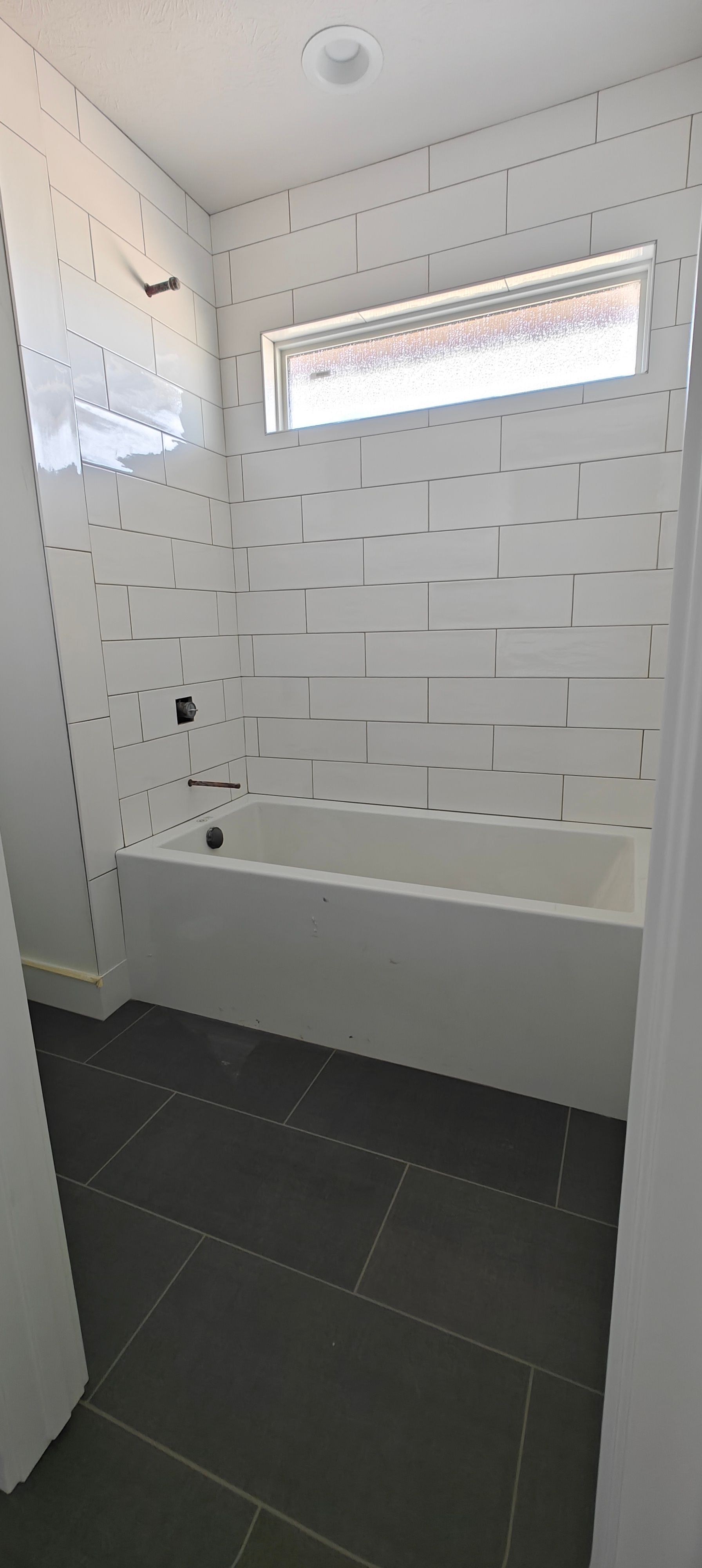 Small bathroom with white tiled tub, narrow window, and dark floor tiles.