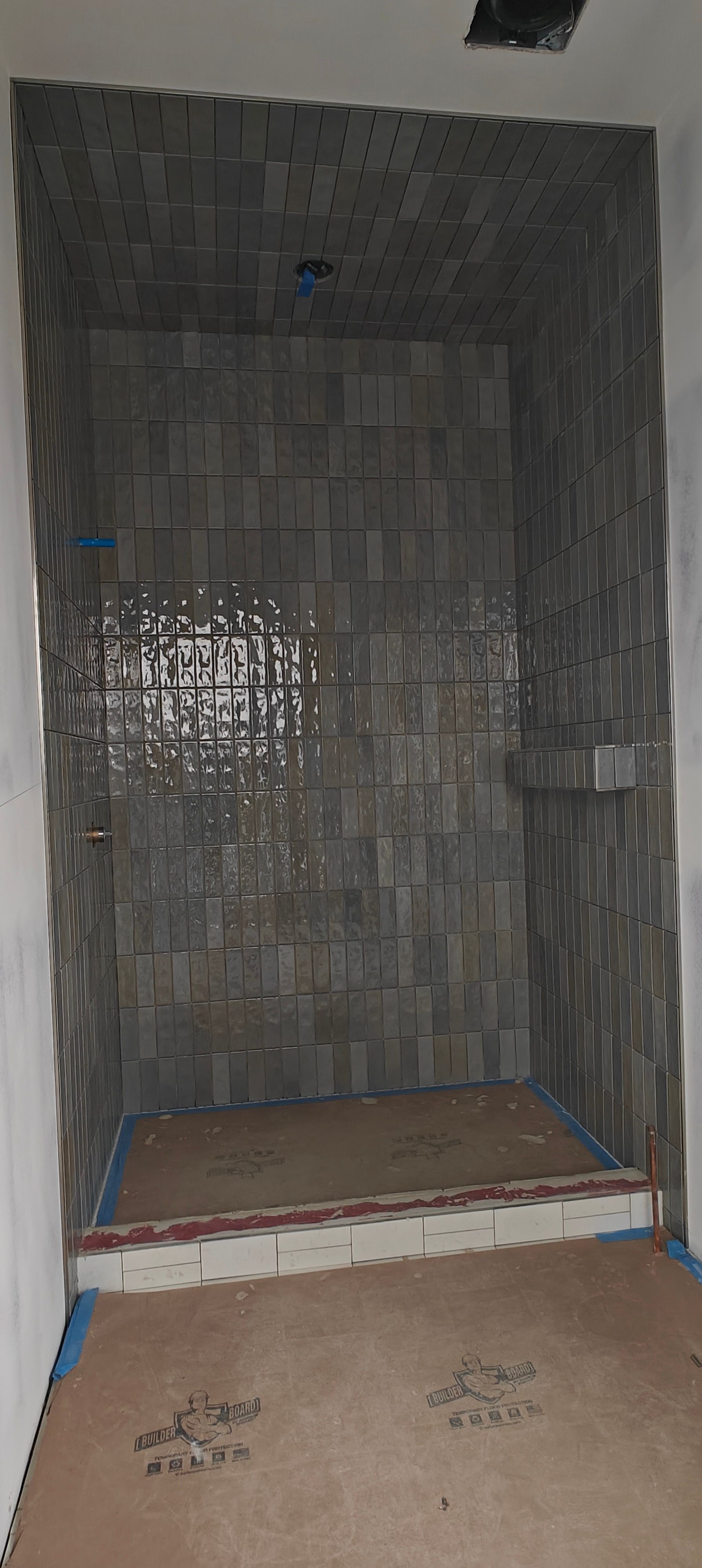Small tiled shower stall under construction, with dark gray walls and a raised threshold.