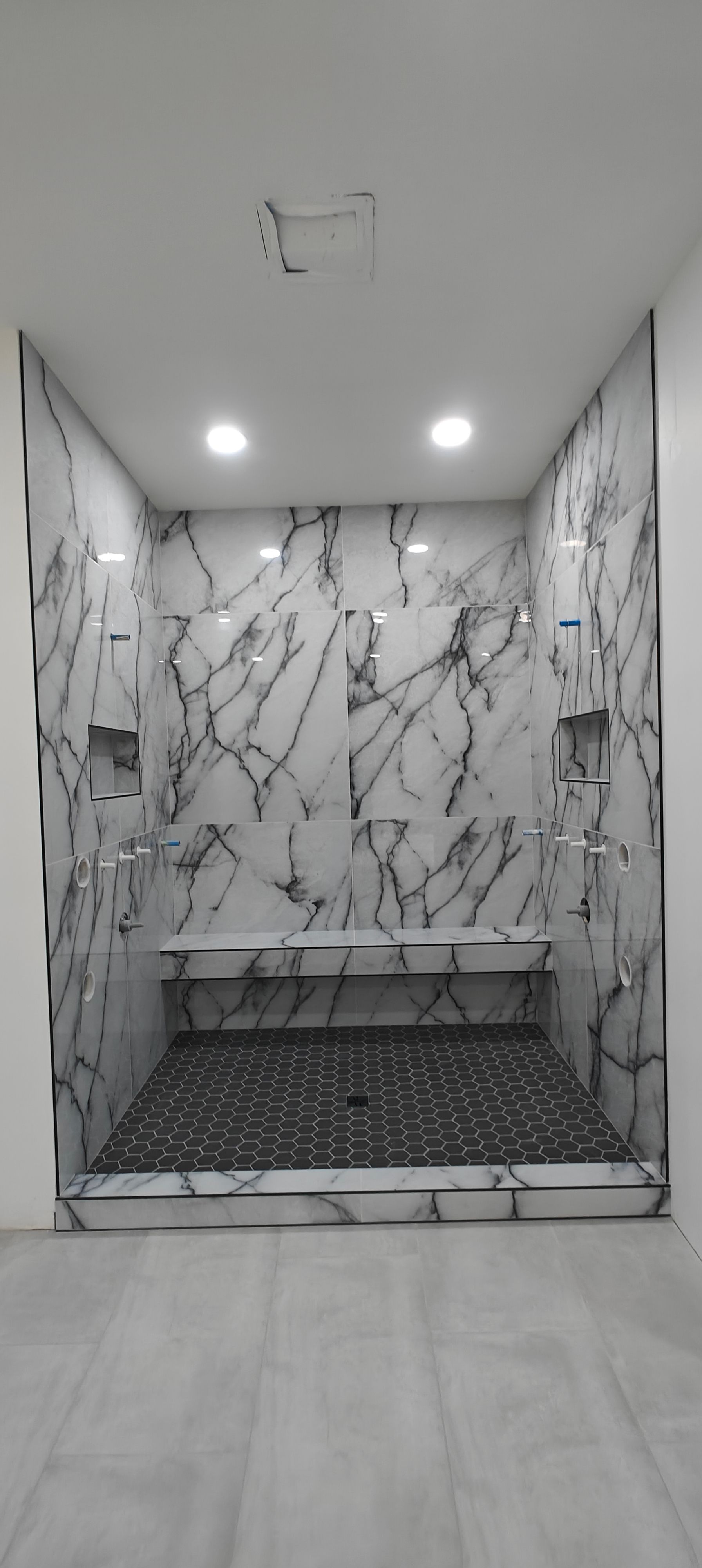 Modern marble-tiled shower stall with recessed lights and black mosaic floor.