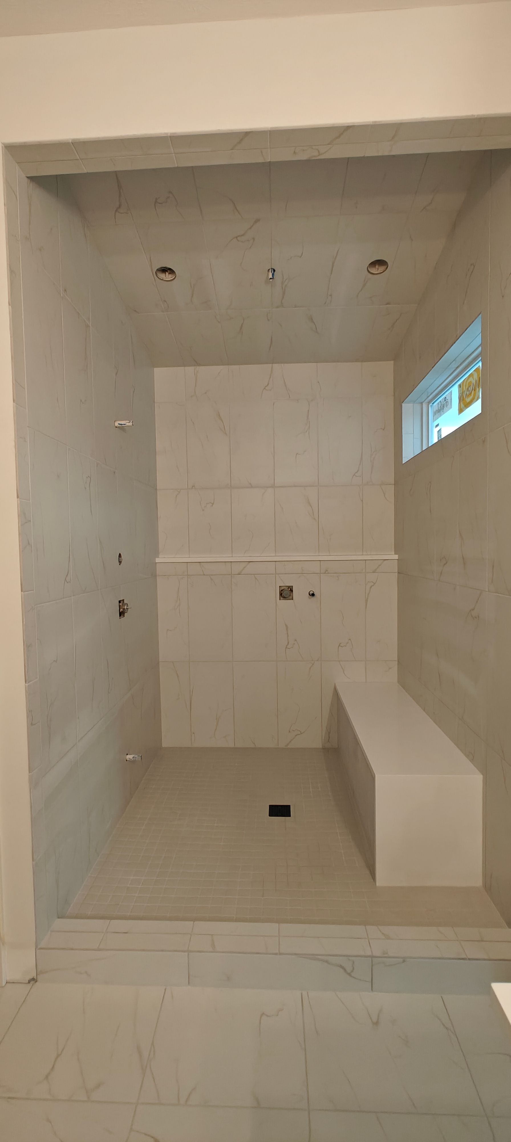 Empty tiled shower stall with built-in bench and small window.