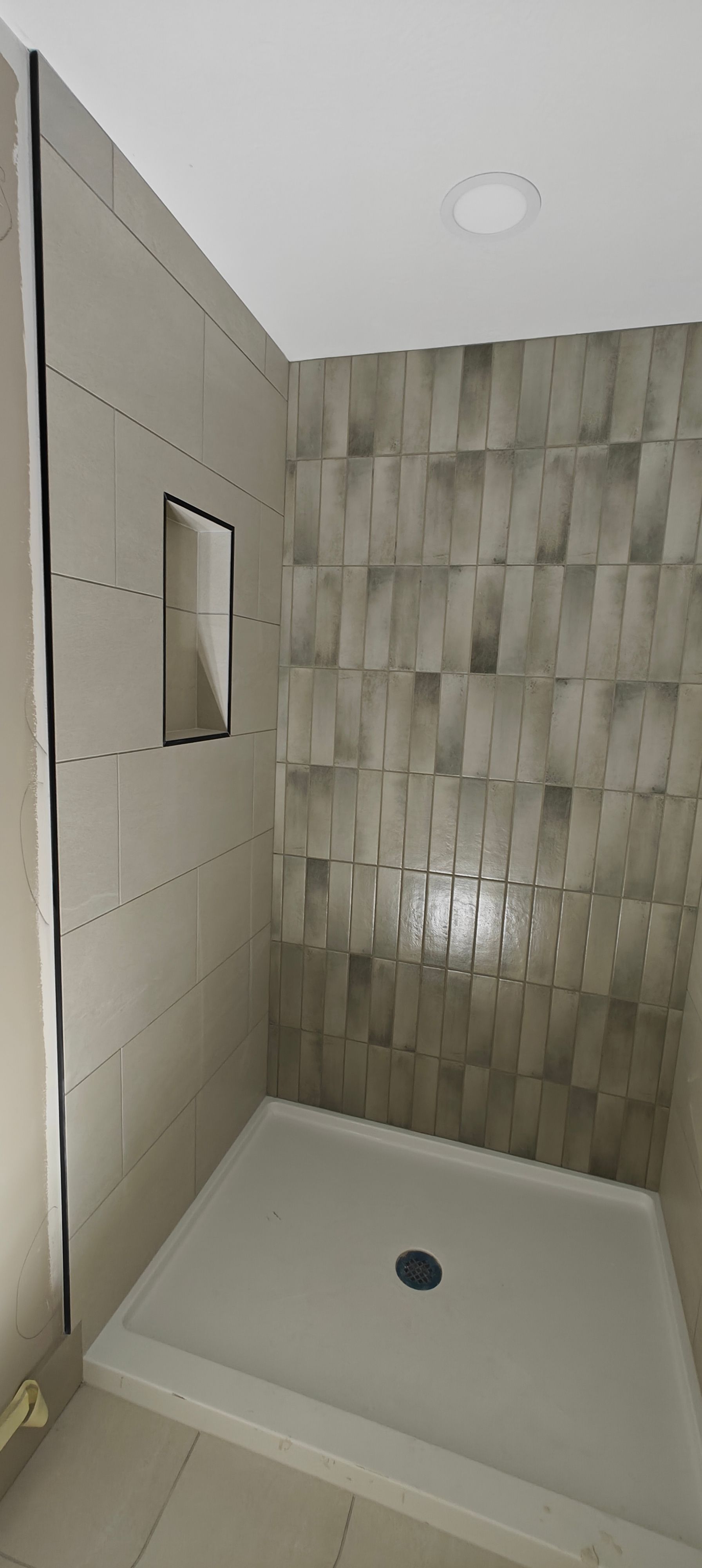 Modern shower stall with beige tiled walls, white base, and a small built-in niche mirror.