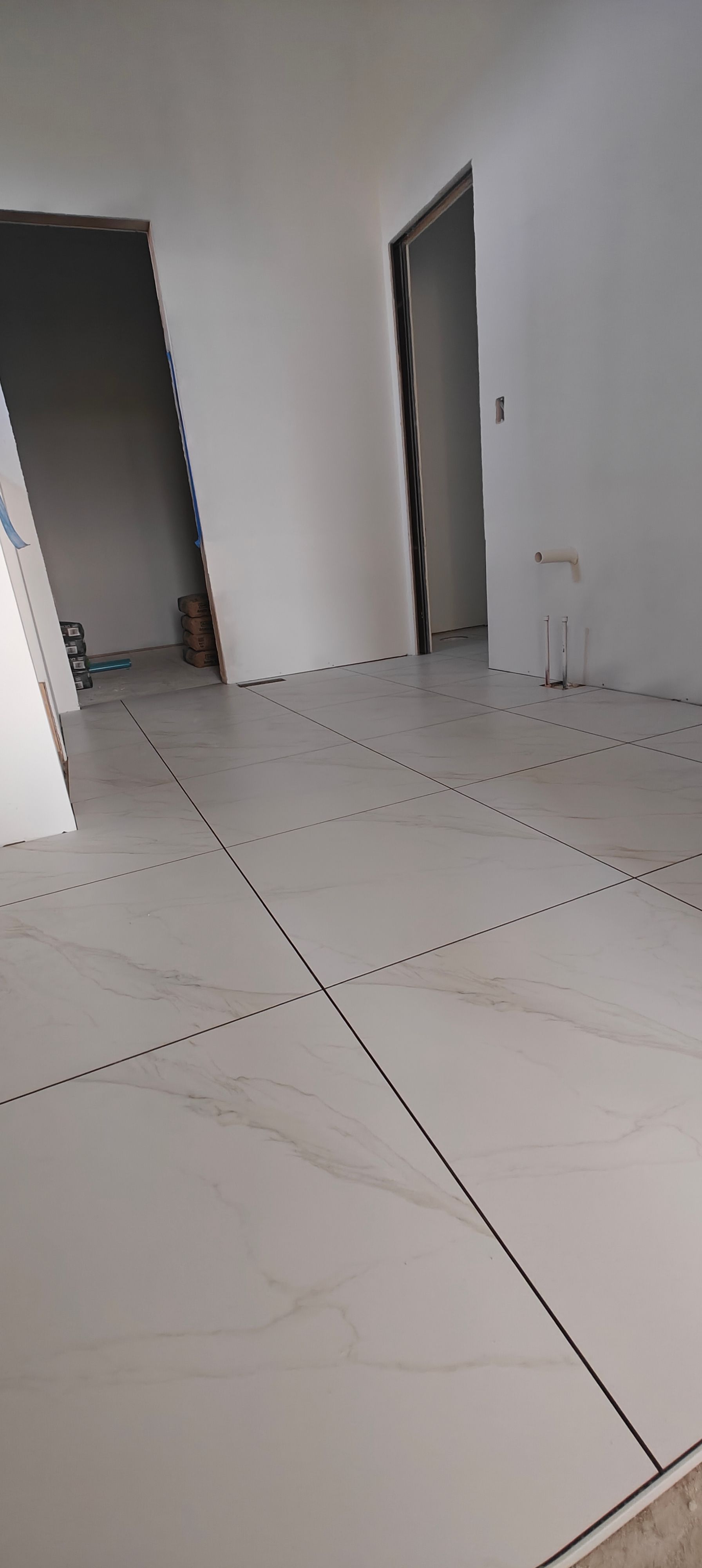 Empty white tiled room with open doorways and a partially visible staircase.