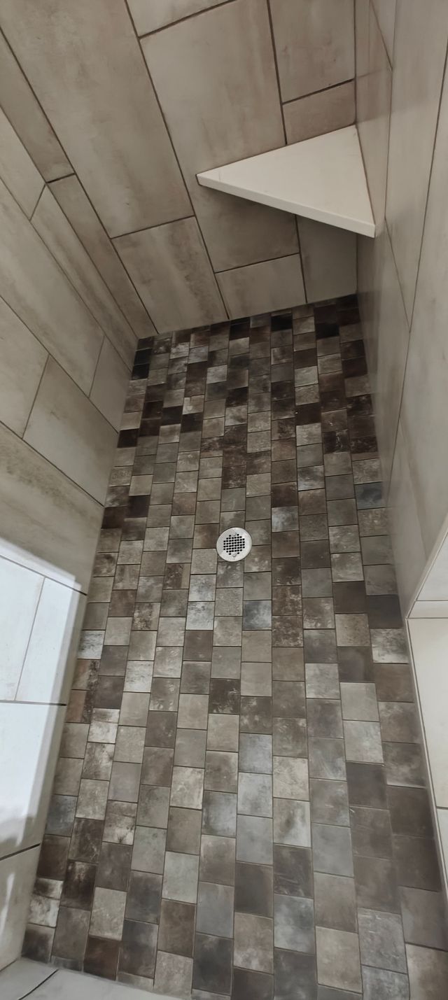 Small bathroom with wood walls, gray tile floor, and a corner shelf above a floor drain.