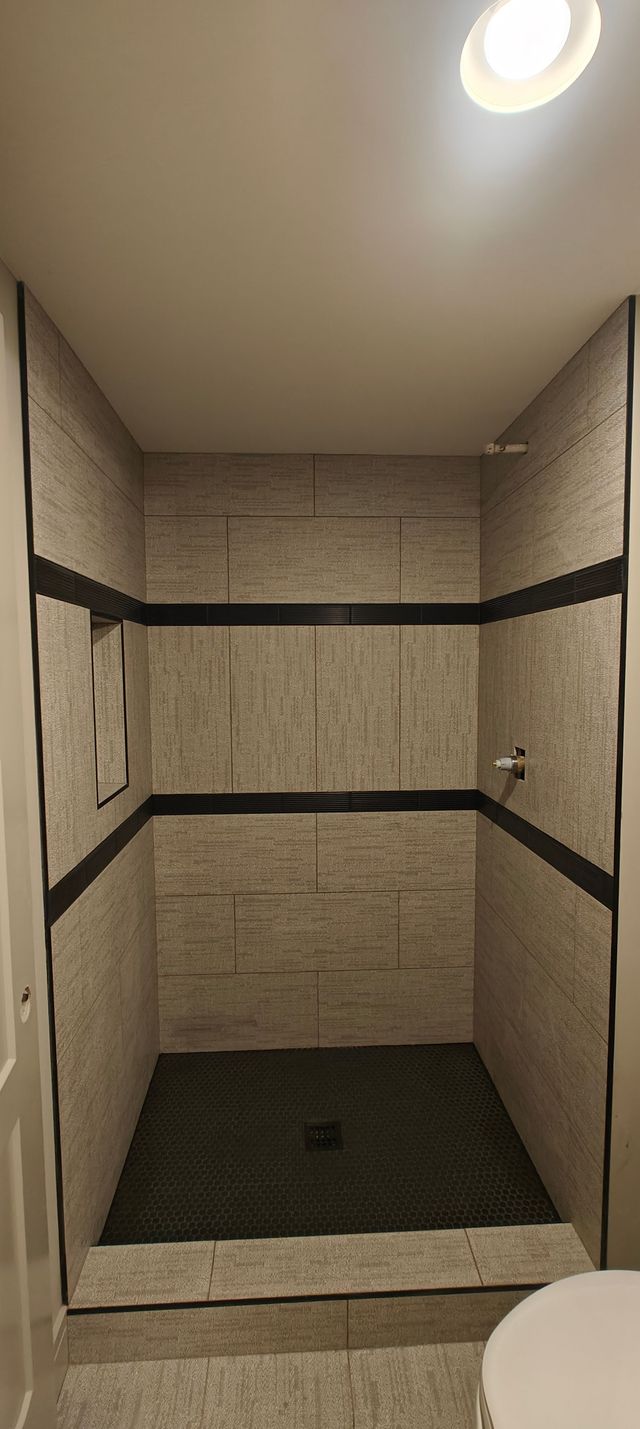Empty tiled shower stall with a dark floor, striped walls, and a ceiling light.