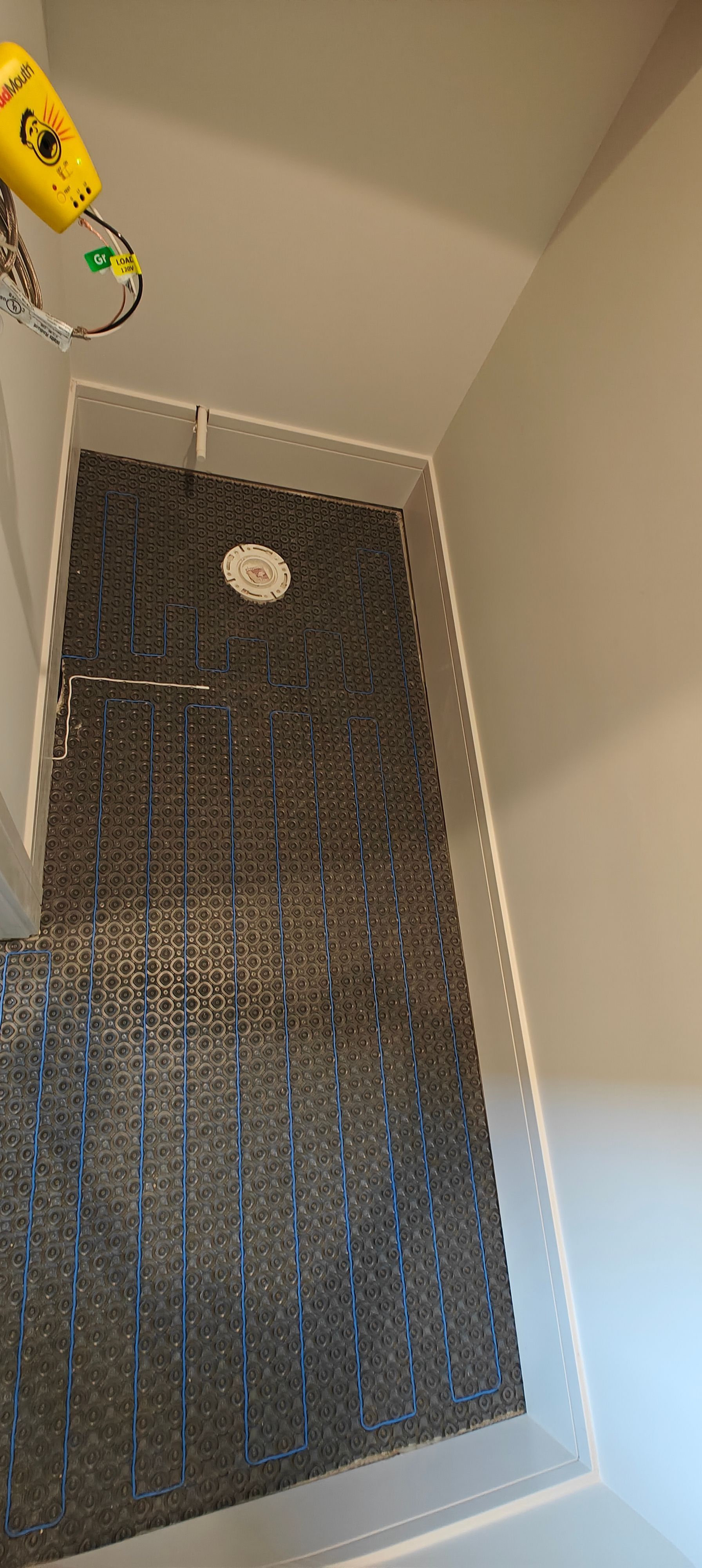 Narrow shower stall with dark pebble-tile floor and a white drain, viewed from above
