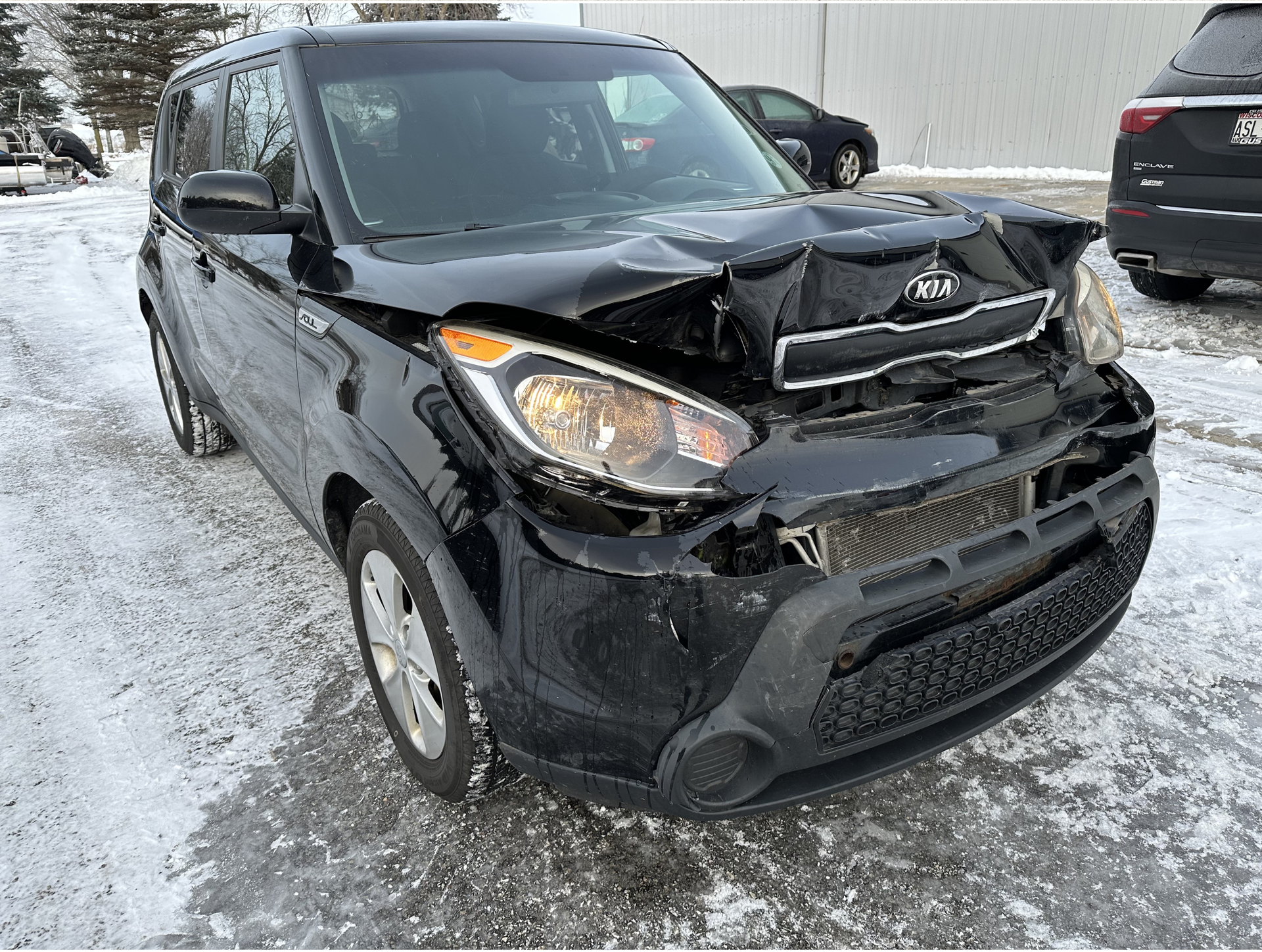 Black Kia Soul with severe front-end damage, in a snowy outdoor setting.
