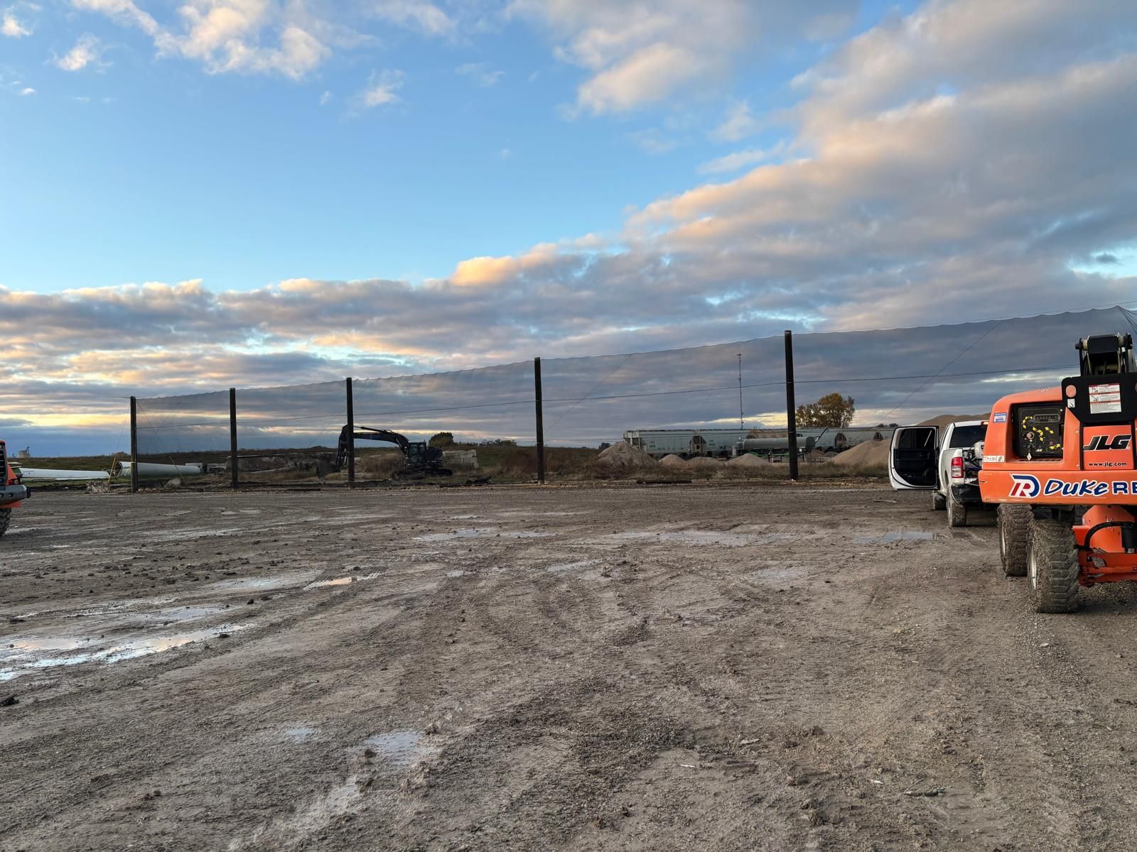 Construction site with dirt ground, utility poles, vehicles, and cloudy sky.