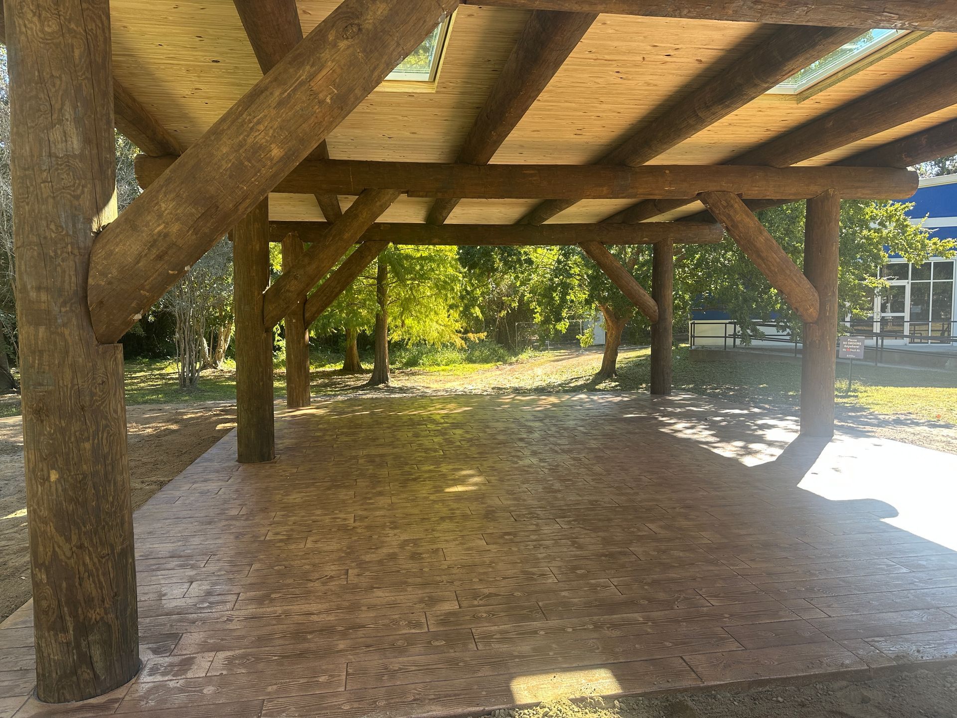 Wooden pavilion with a concrete floor, surrounded by trees and greenery.